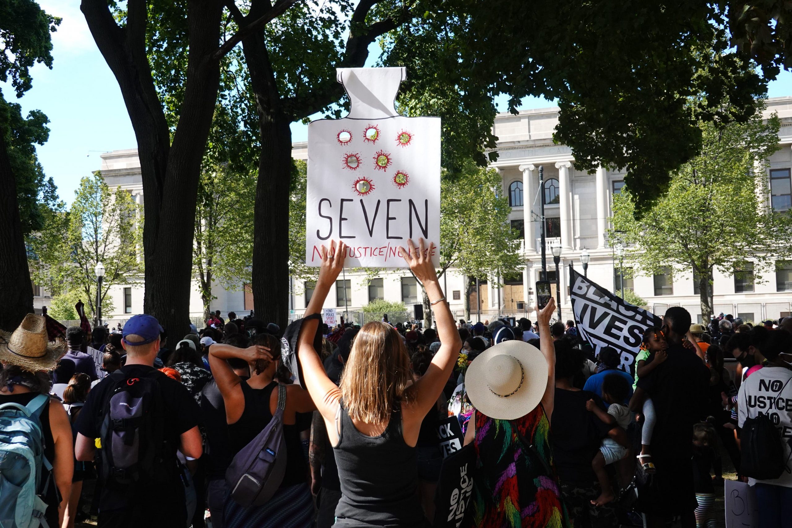 a woman holds a sign with bullet holes in it and the word seven at a rally supporting jacob blake