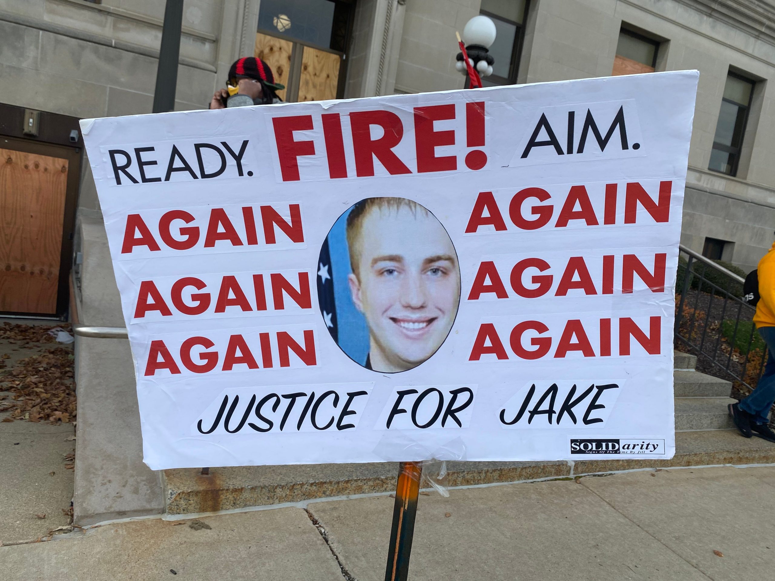 a sign says ready fire! aim. again again again again again again justice for jake