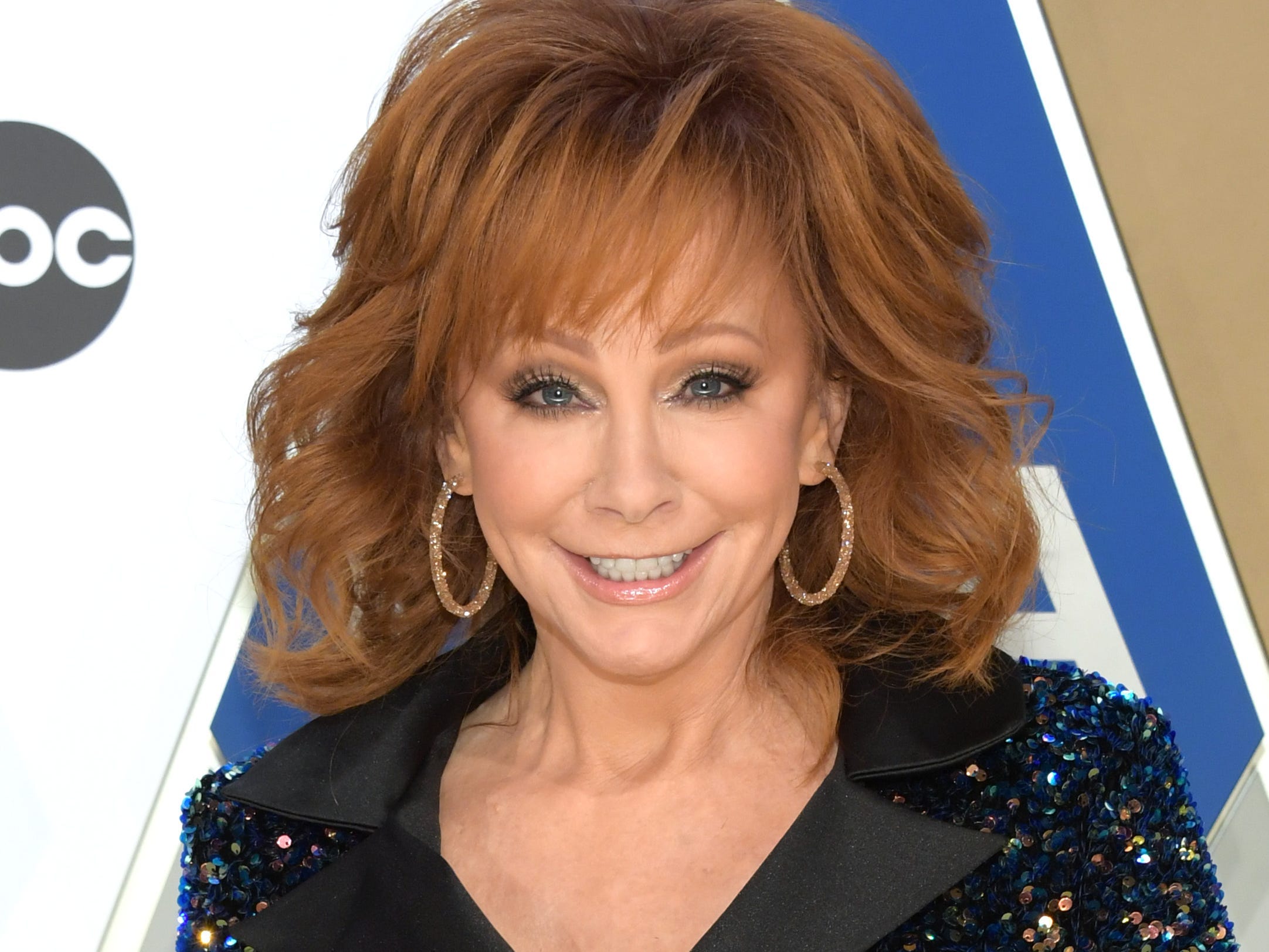 Reba McEntire in a sparkly black suit and big hoop earrings.