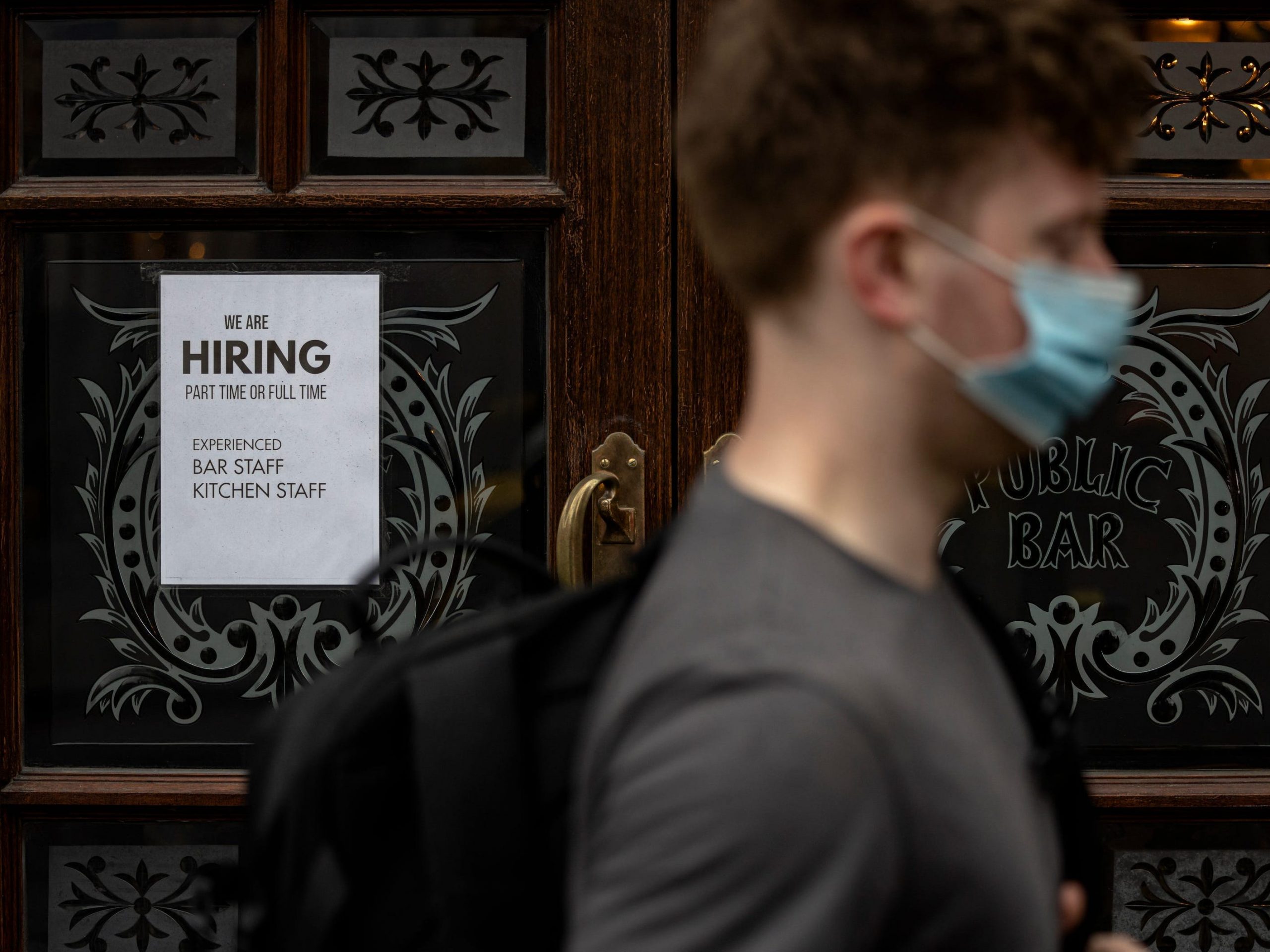 A man wearing a face mask walks past a recruitment sign in the window of a pub in Westminster on June 04, 2021 in London, England.