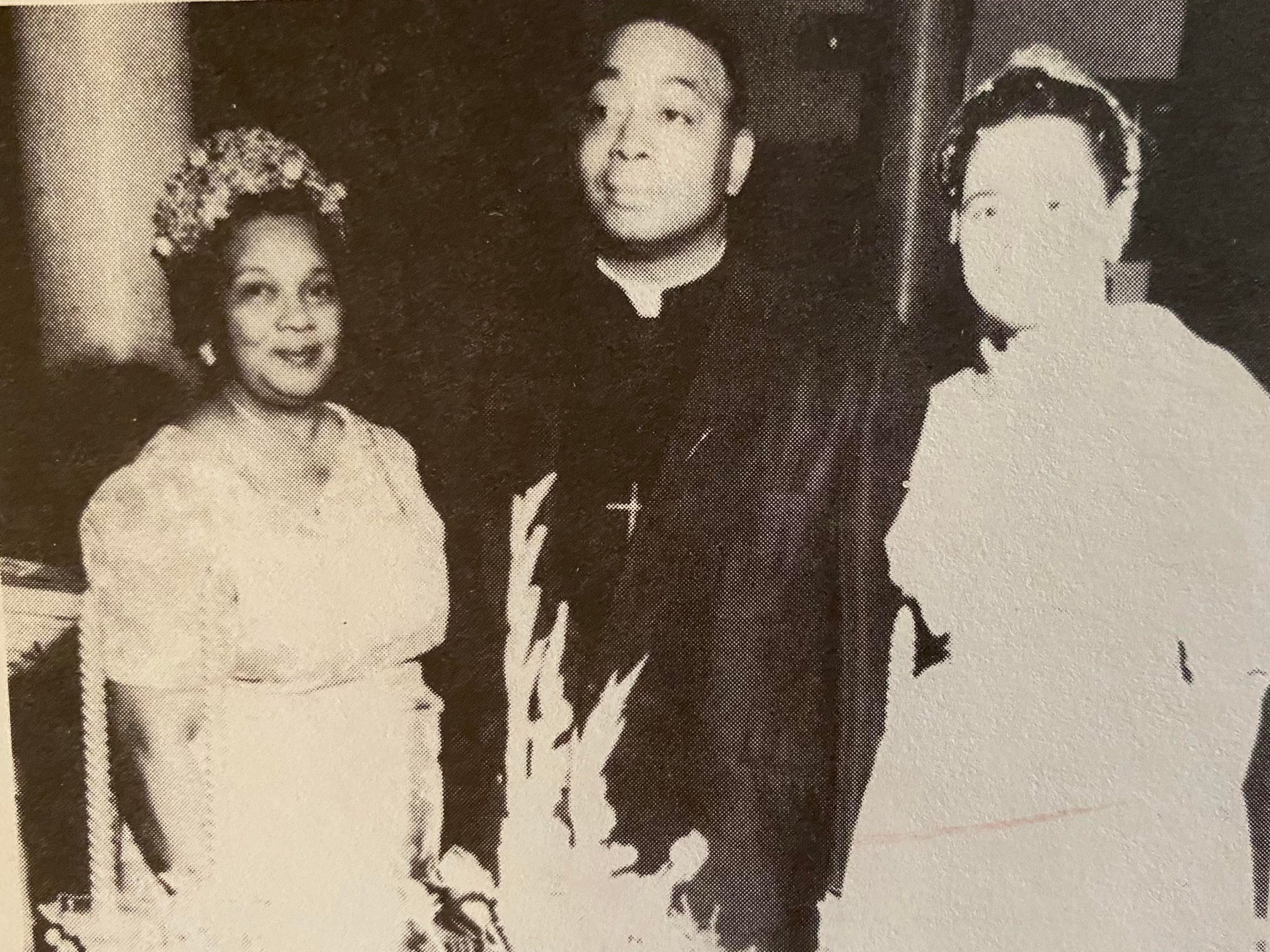 a woman wearing church clothes and a fancy hat poses with a reverend and another woman in white