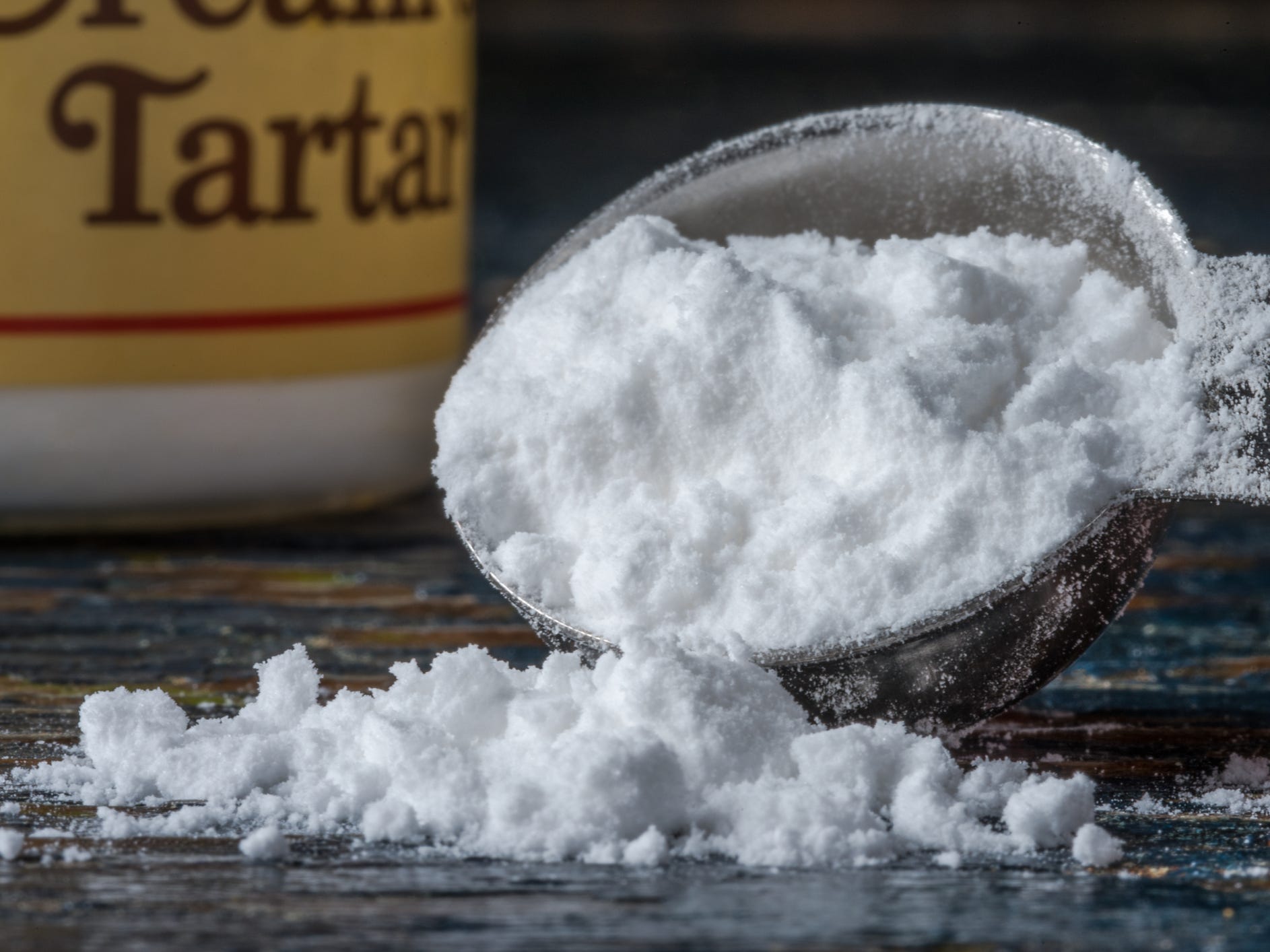 A tablespoon of cream of tartar spilling onto a black counter