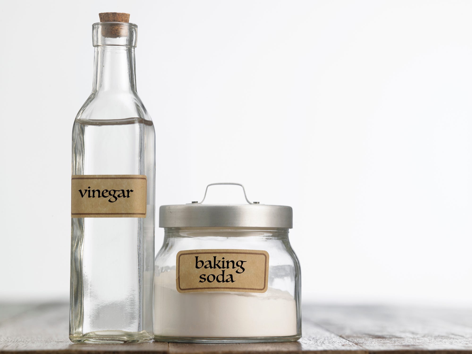 A tall glass bottle labeled "vinegar" next to a short glass jar labeled "baking soda"