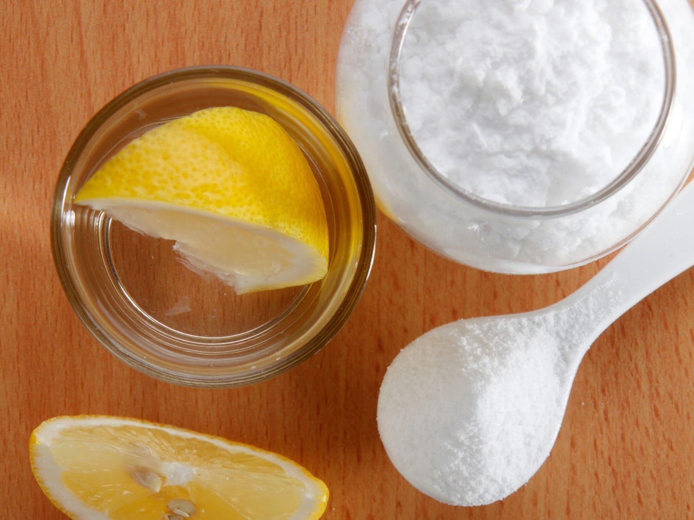 A lemon wedge in a small glass bowl next to a glass jar and spoonful of baking powder