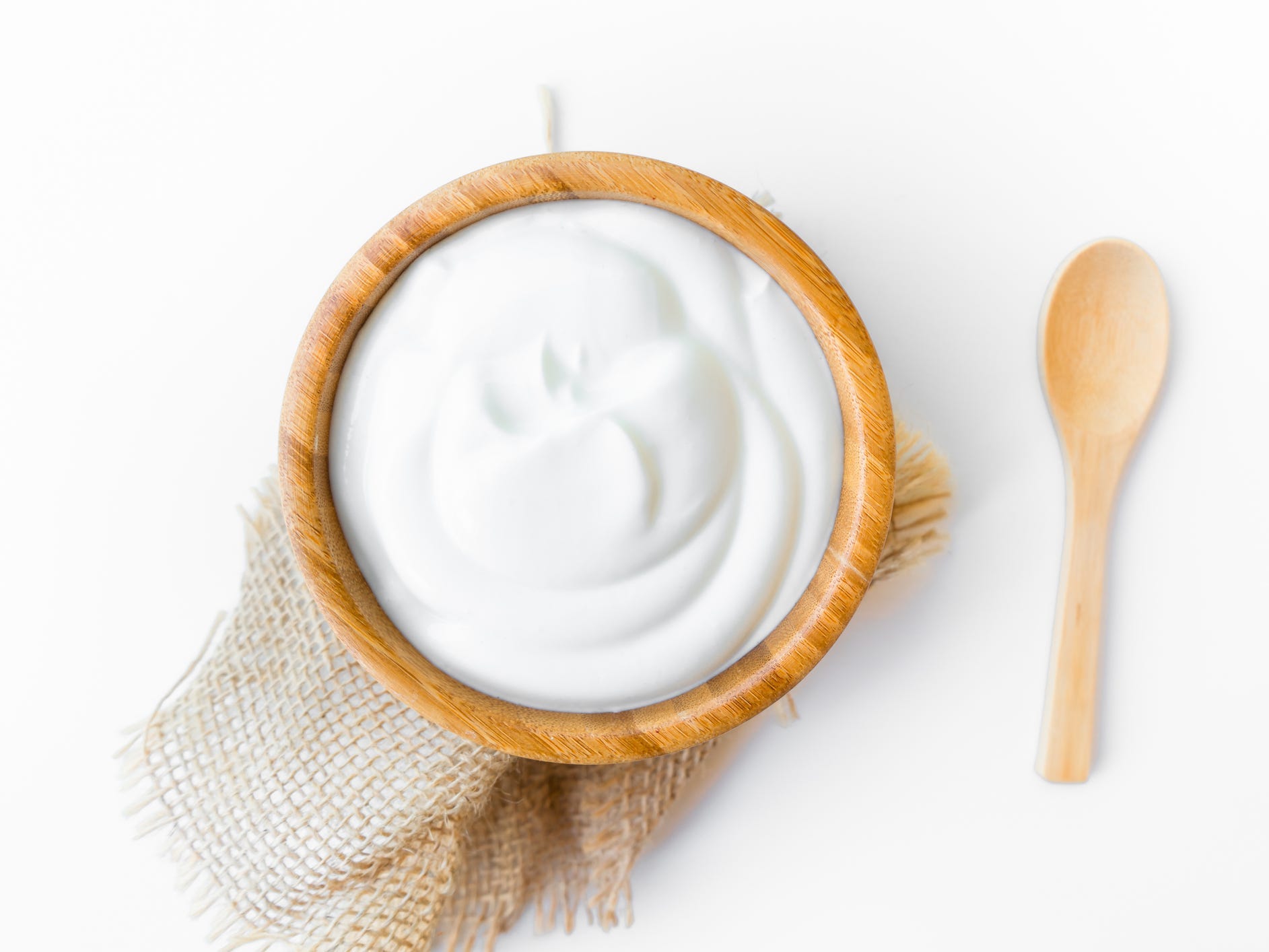 A wooden bowl full of yogurt sitting on burlap fabric with a wooden spoon next to it