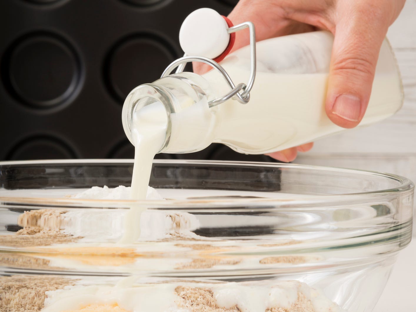 Buttermilk being poured out of a glass bottle into a bowl of baking ingredients