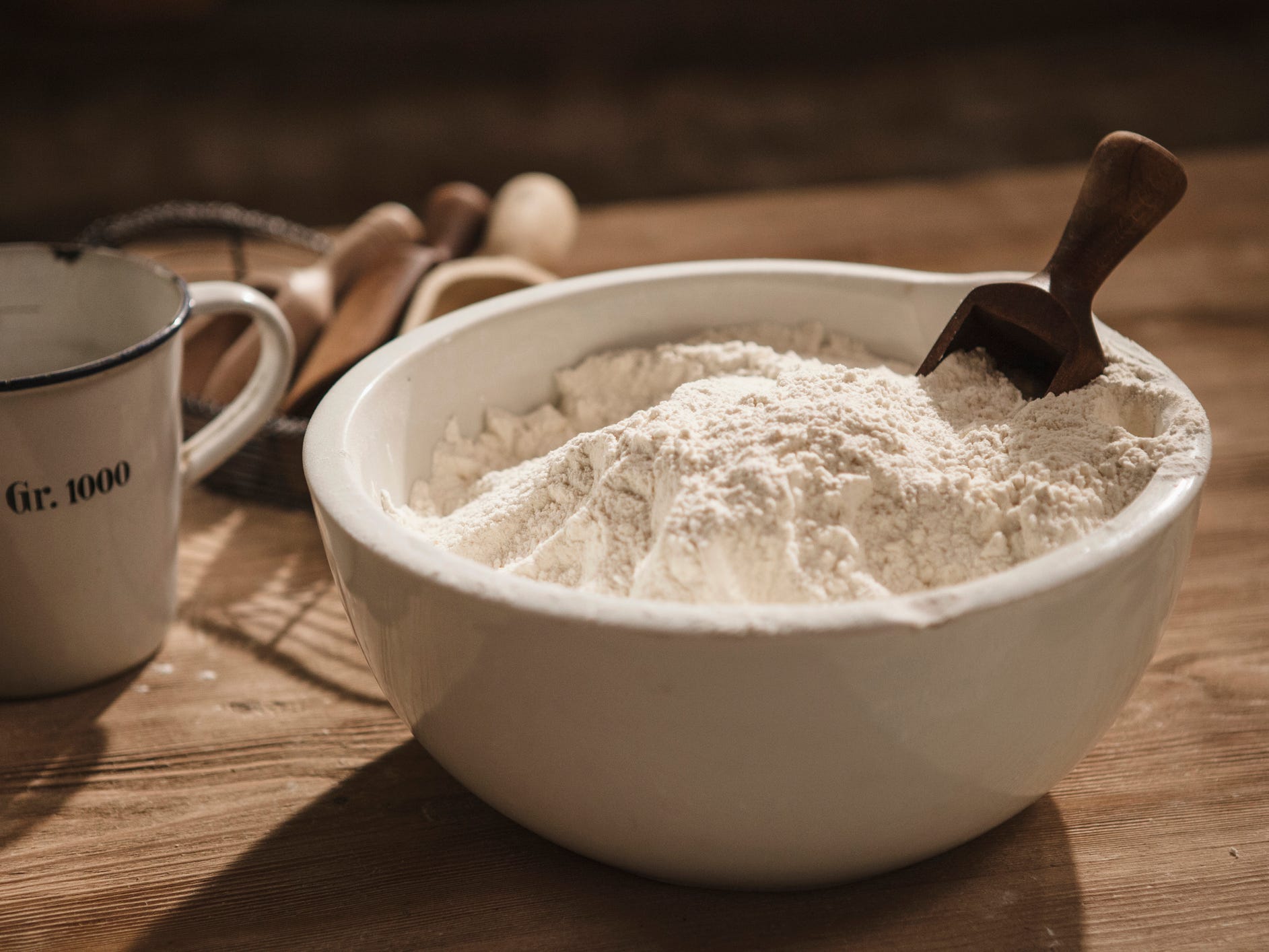 A large white ceramic bowl of flour with a small wooden scoop in it