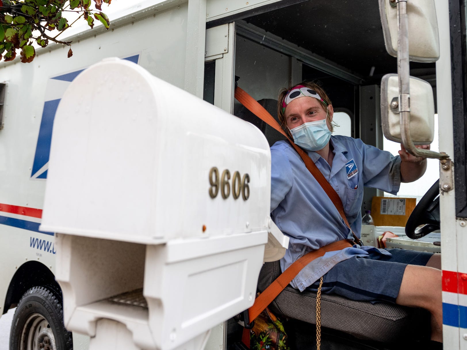 A USPS worker wearing a mask puts envelopes in a mailbox.
