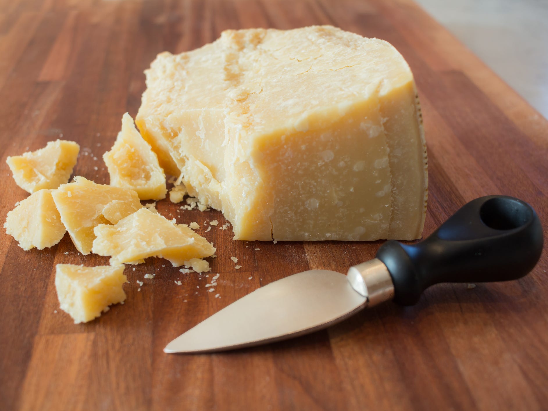 A wedge of Parmigiano Reggiano broken into chunks with a cheese knife sitting in front