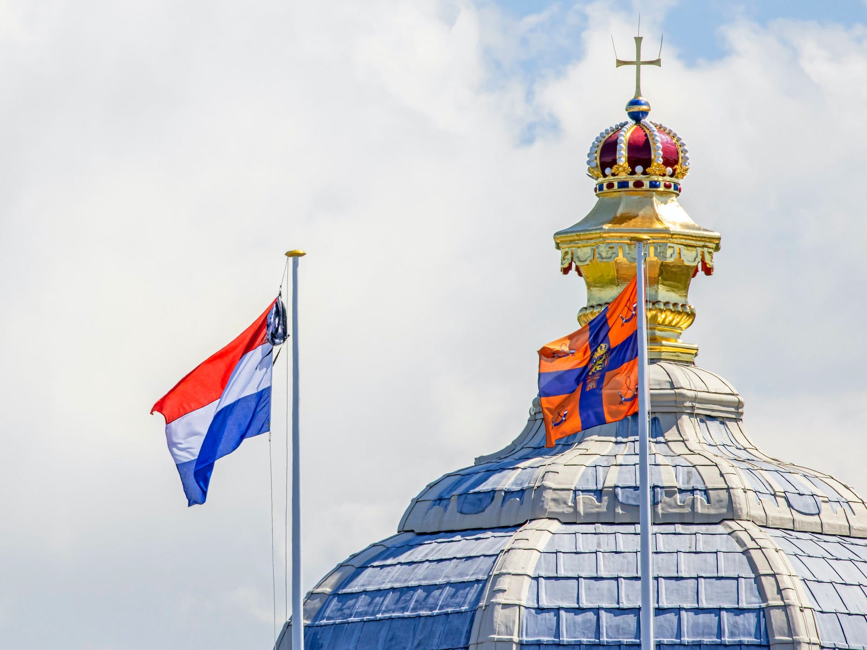 A backpack hangs on the same pole as the Dutch flag in front of the Palace Huis ten Bosch.