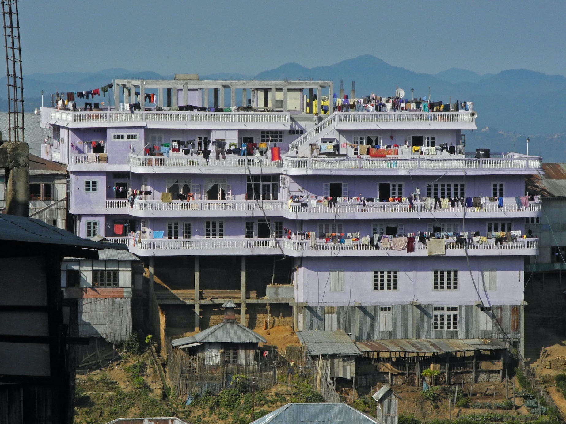 A four-story purple house full of people in front of mountains.