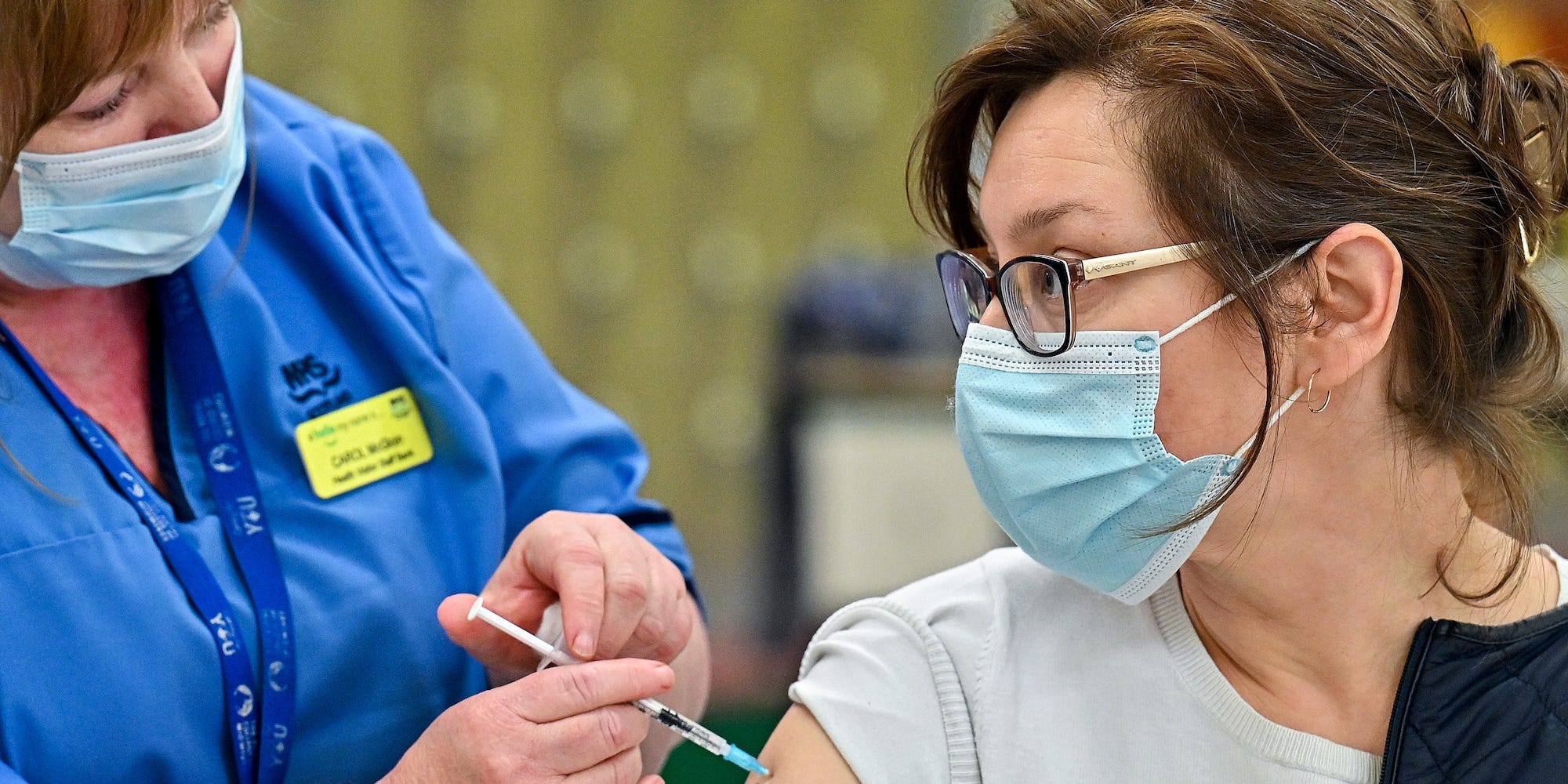 A health professionals gives a woman wearing a mask a COVID-19 vaccine in the arm in Scotland.