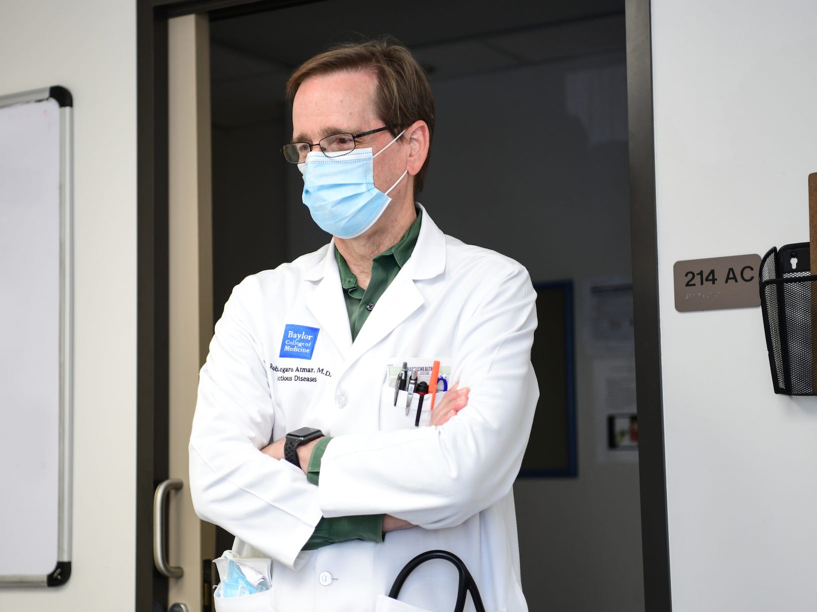 dr. robert atmar stands with his arms crossed and lab coat on
