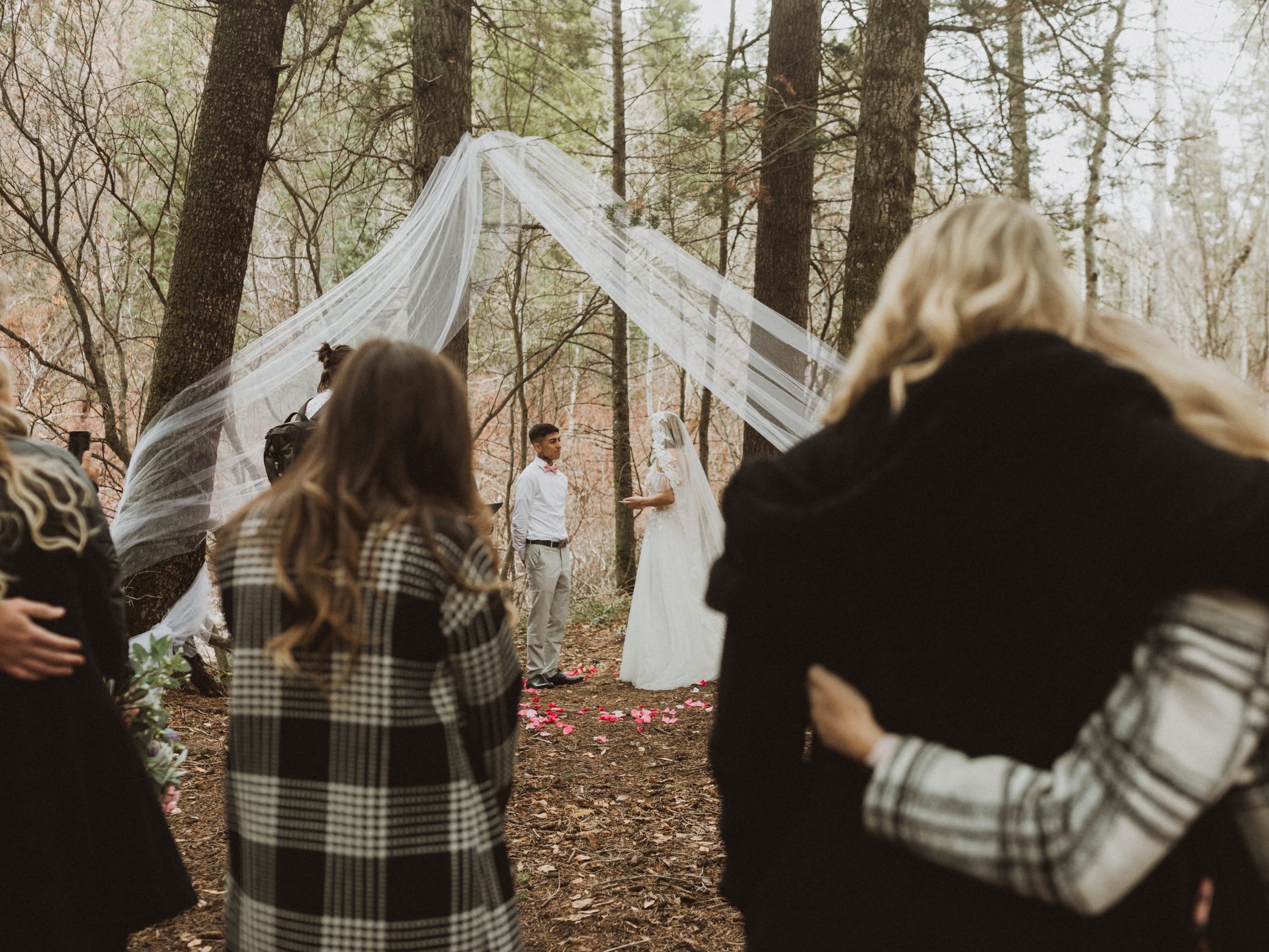 guests standing in front of a bride and groom getting married in a forest