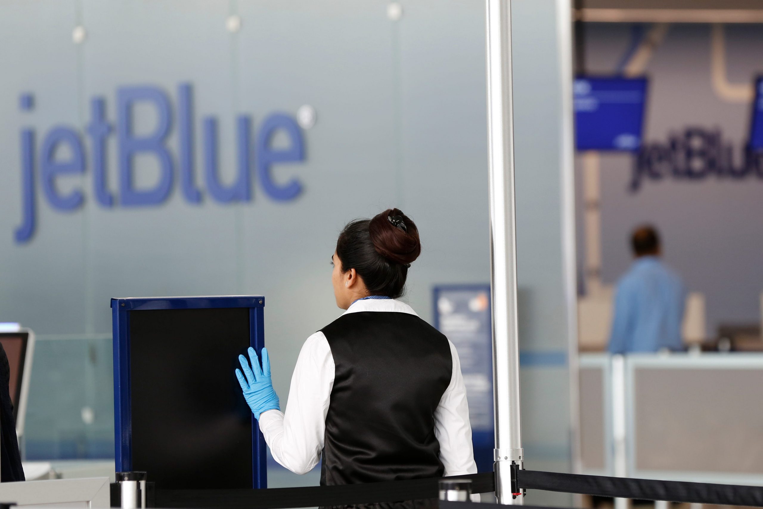 A TSA employee raises her hand to stop passengers in front of a JetBlue sign