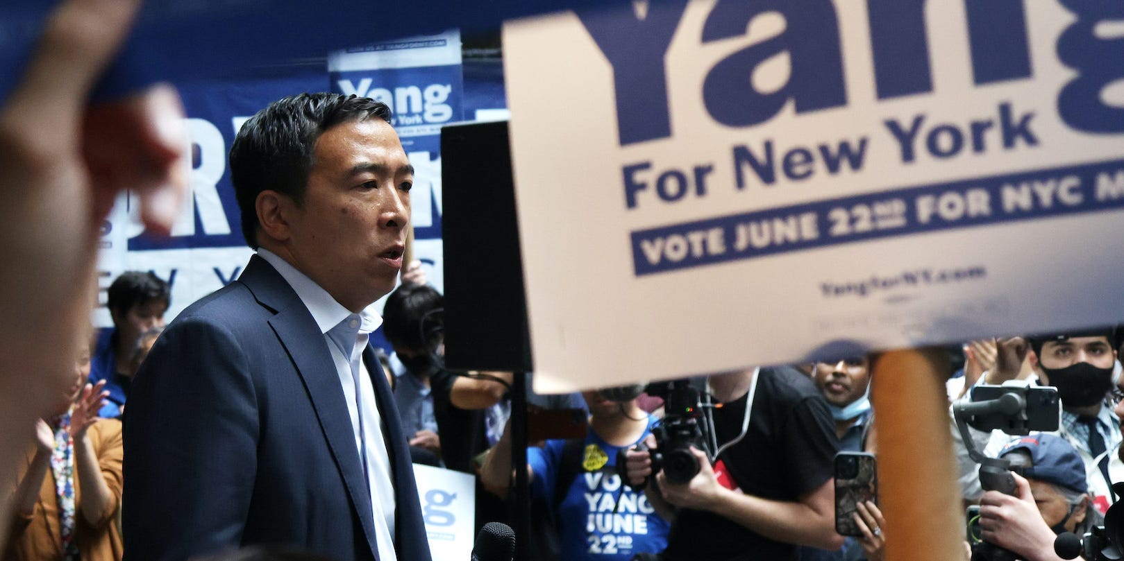 Democratic New York City mayoral candidate Andrew Yang stands at a campaign rally surrounded by supporters waving signs.