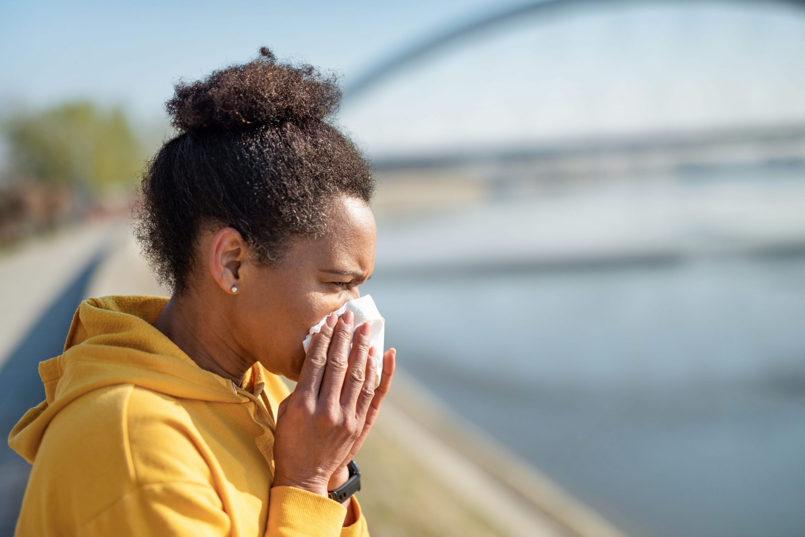 A woman sneezing while out for a run.