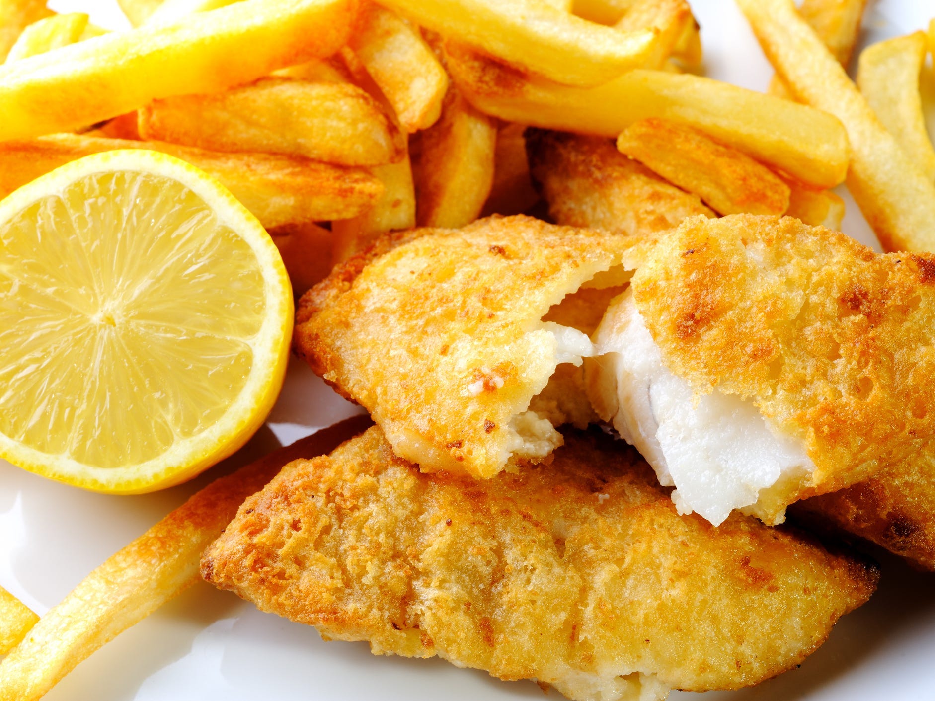 Fried white fish on a plate with a lemon half and french fries