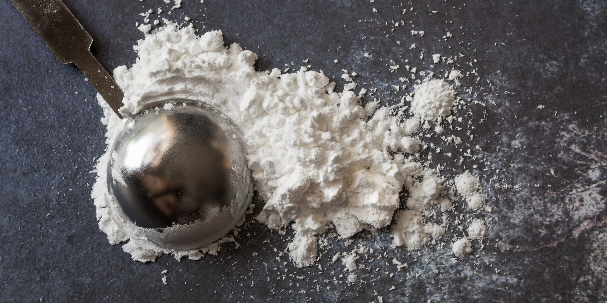 Cornstarch spilled on a black counter with an overturned teaspoon on top