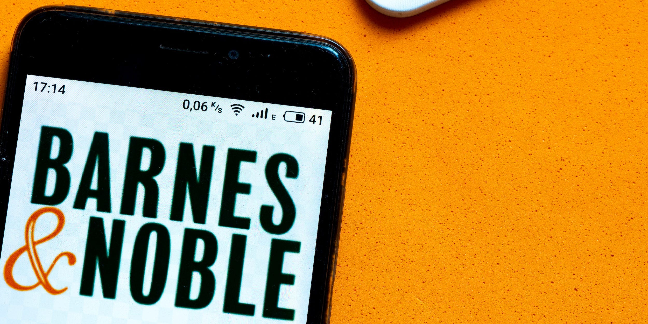 Barnes & Noble logo on a smartphone next to laptop keyboard on orange background