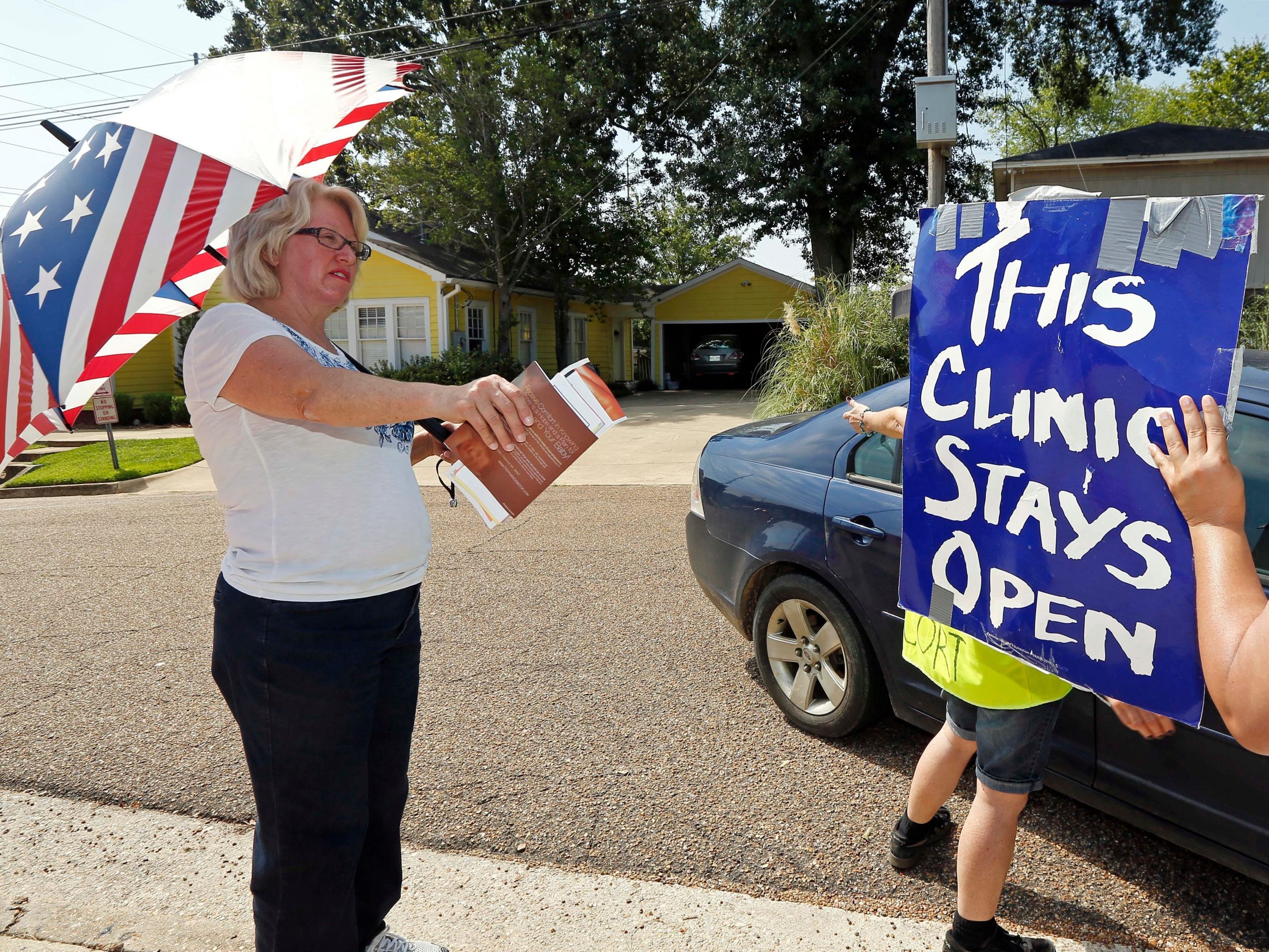 In this Aug. 15, 2013 photograph, abortion opponent Mary McLaurin, left, shielding herself from the strong sunlight with an umbrella, challenges clinic defenders who have blocked her sidewalk access from a car transporting a patient to the Jackson Women's Health Organization Clinic in Jackson, Miss. McLaurin, a long time abortion opponent, has provided sidewalk counseling once a week for two years, asking the patients to reconsider abortions and to discuss with her alternatives to the medical procedure. The clinic is the only facility in Mississippi that provides abortions. The Abortion Rights Freedom Ride, a group of more than a dozen people traveling to states that have few clinics or that are enacting laws that would restrict access to the procedure are to "defend" the facility Saturday, Aug. 17, with a rally.