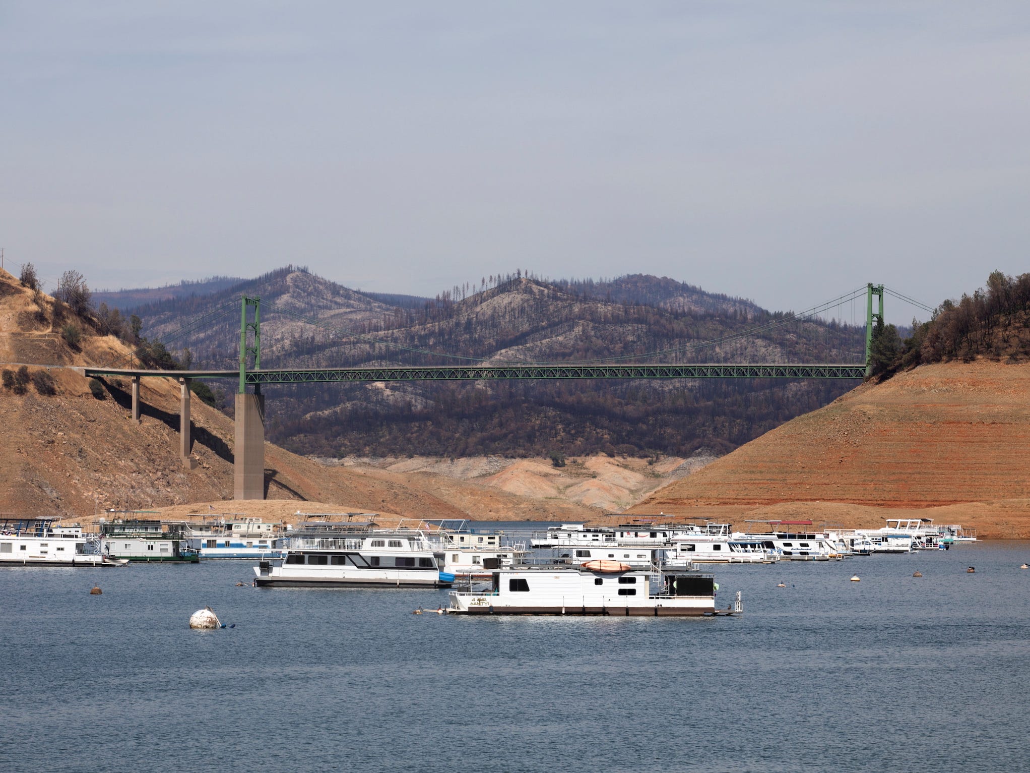 houseboats sit at low water levels in lake oroville below a bridge with exposed lake bottom