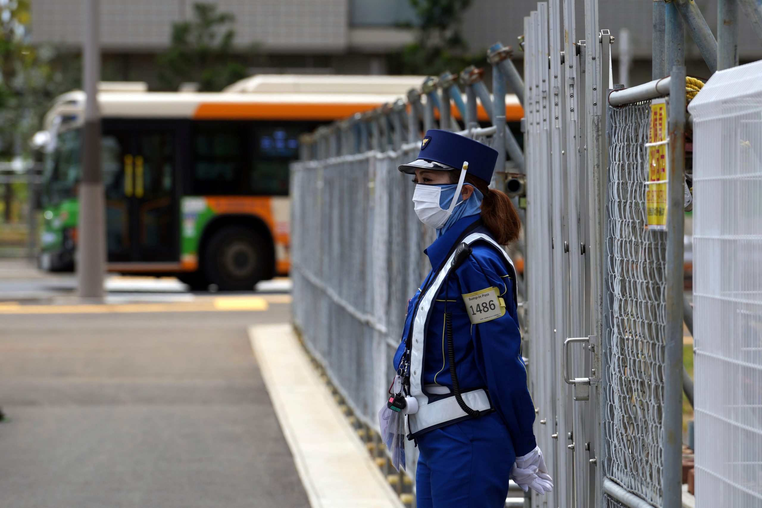 A guard in blue stands in front of the Tokyo Olympics Athletes Village fence