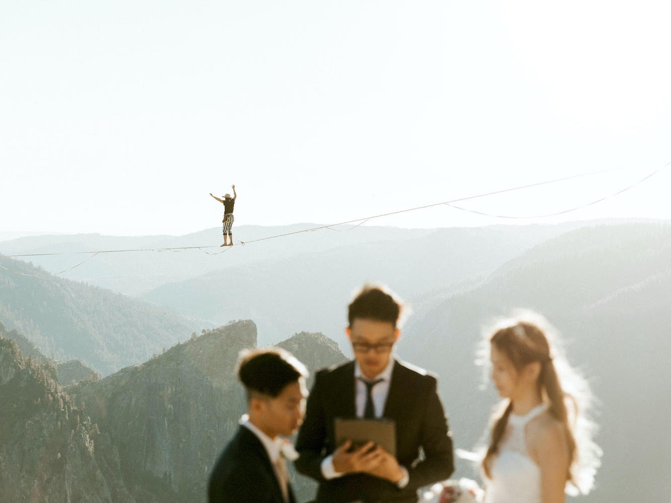 A person walks on a tightrope behind a couple getting married.