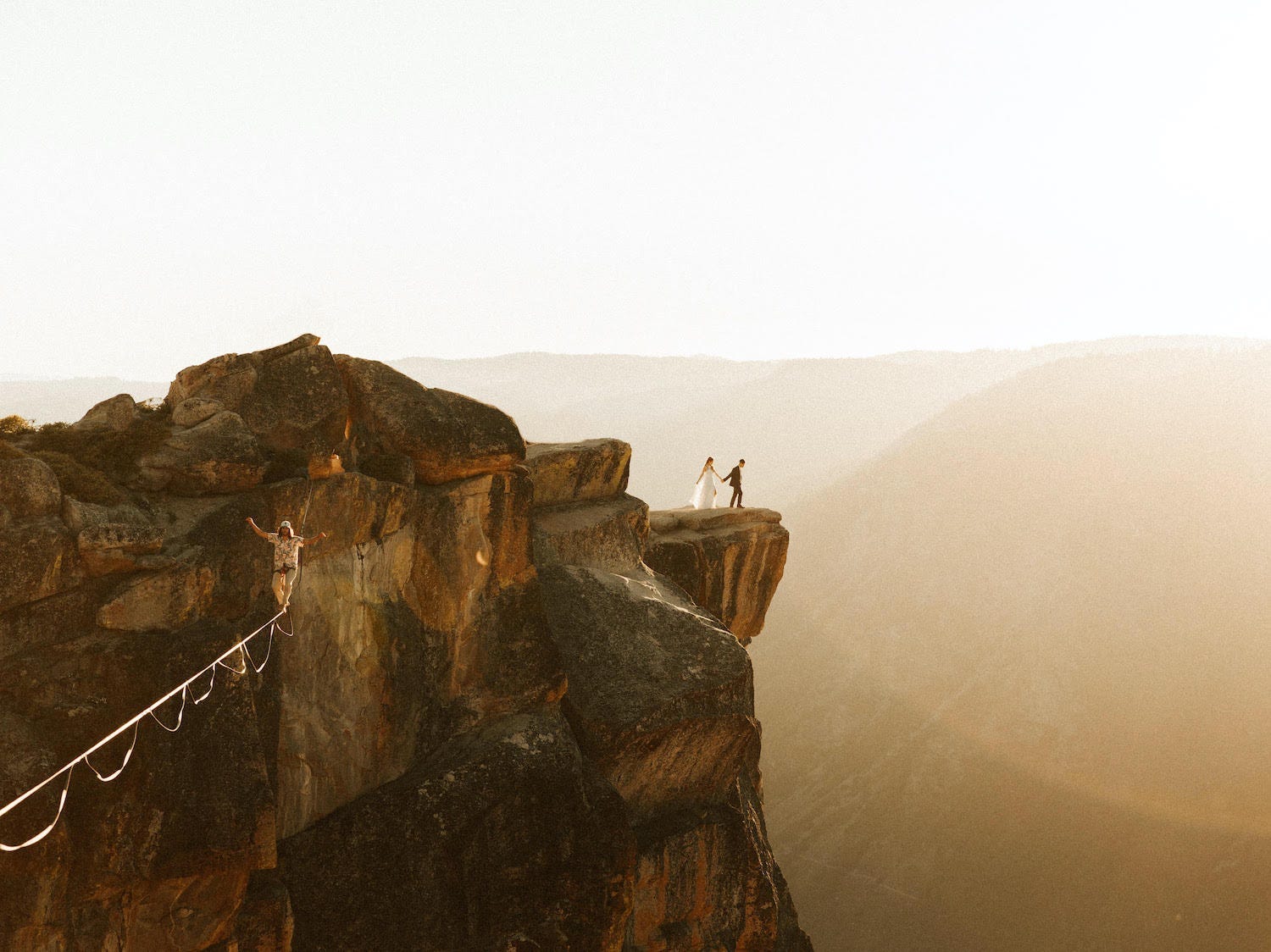 A slackliner is spotted in the forefront with a wedding couple in the background of Yosemite National Park.