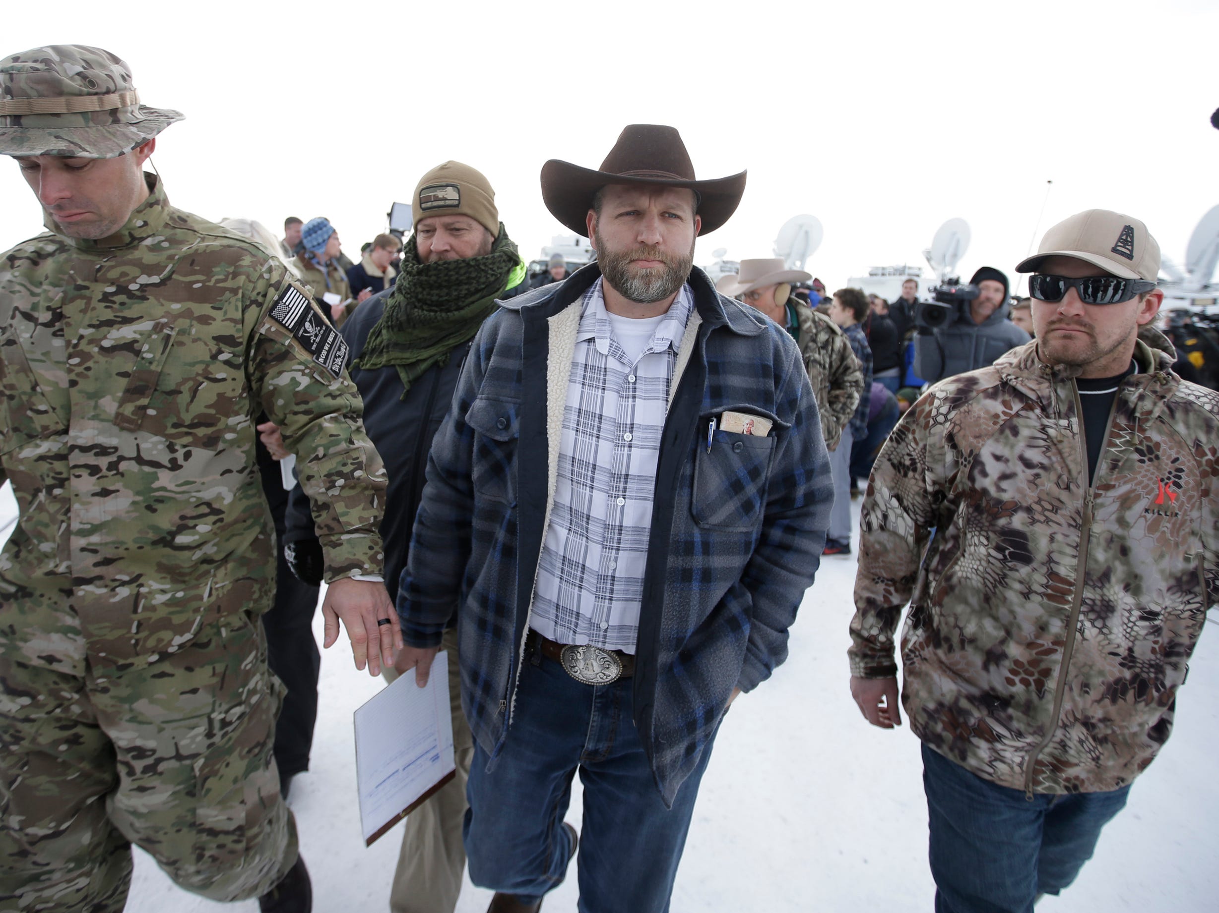Ammon Bundy, wearing a cowboy hat, walks between two law enforcement agents.