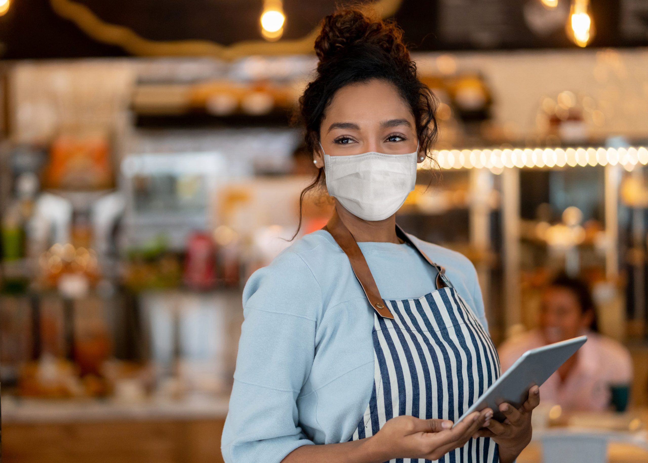 A restaurant worker wears a facemark while holding a tablet to take customer orders.