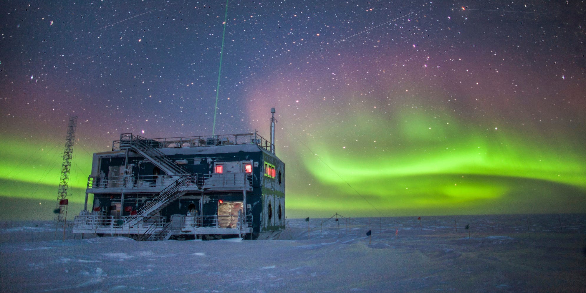 The Atmospheric Research Observatory,  two-storied industrial building, is pictured here at night in 2018 in front of green auroras lighting up the sky in the background.