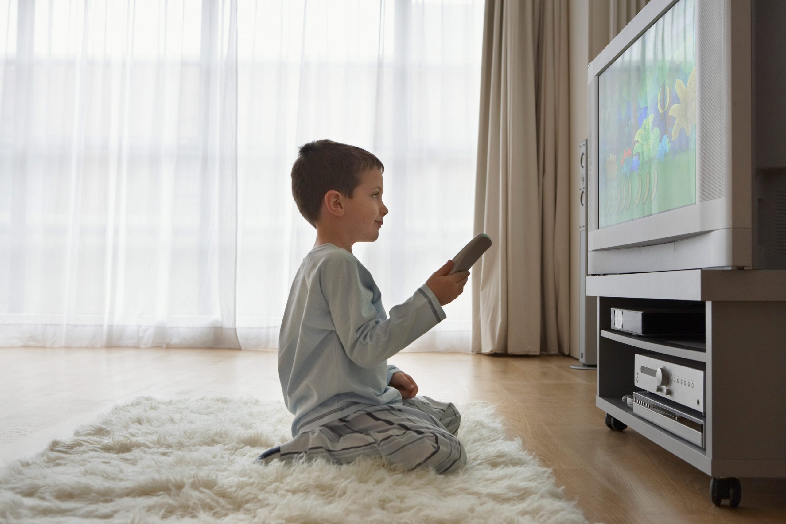 A child sitting on the floor and holding a remote while watching TV