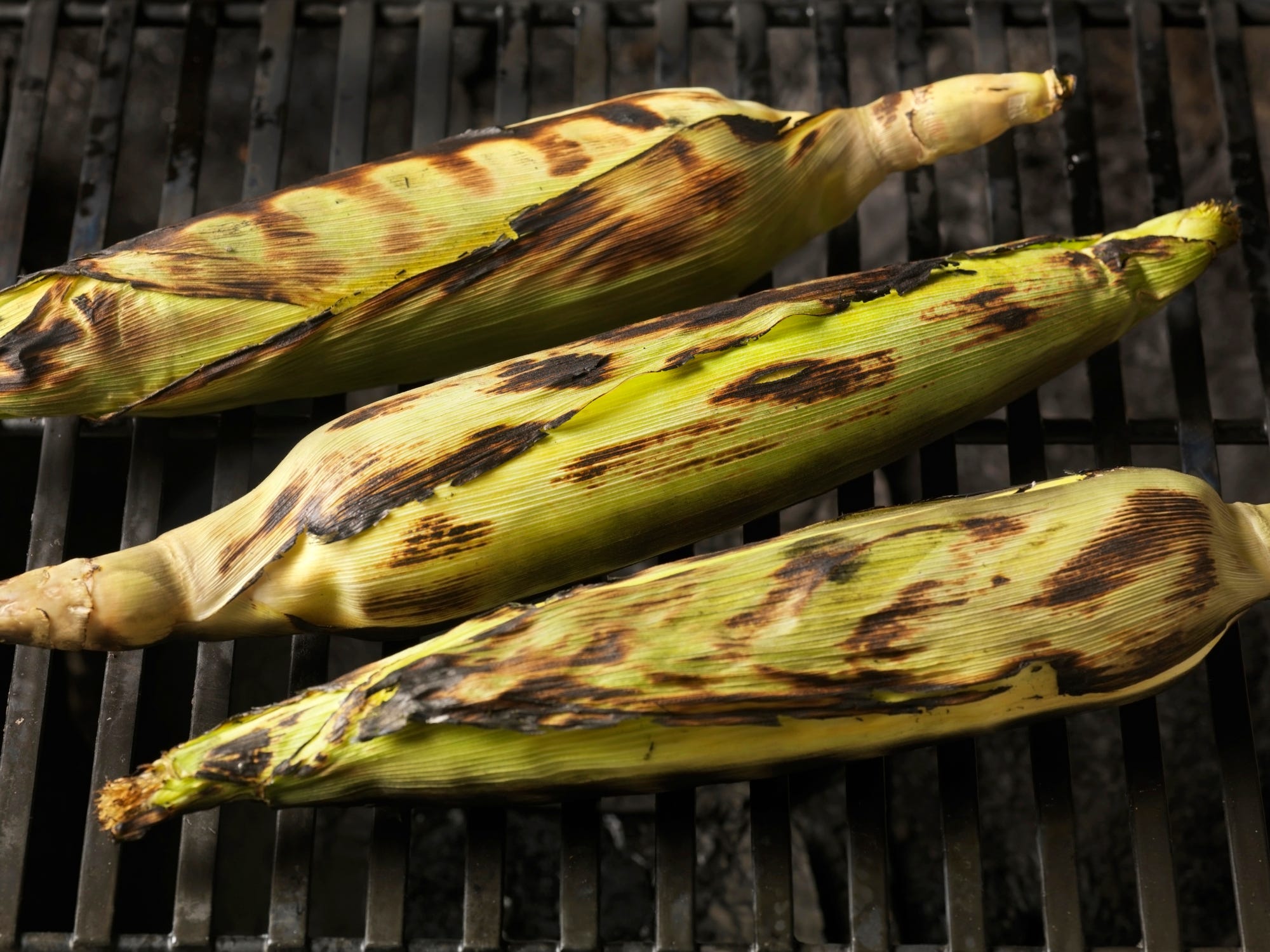 Three ears of corn on the grill with the husks still on