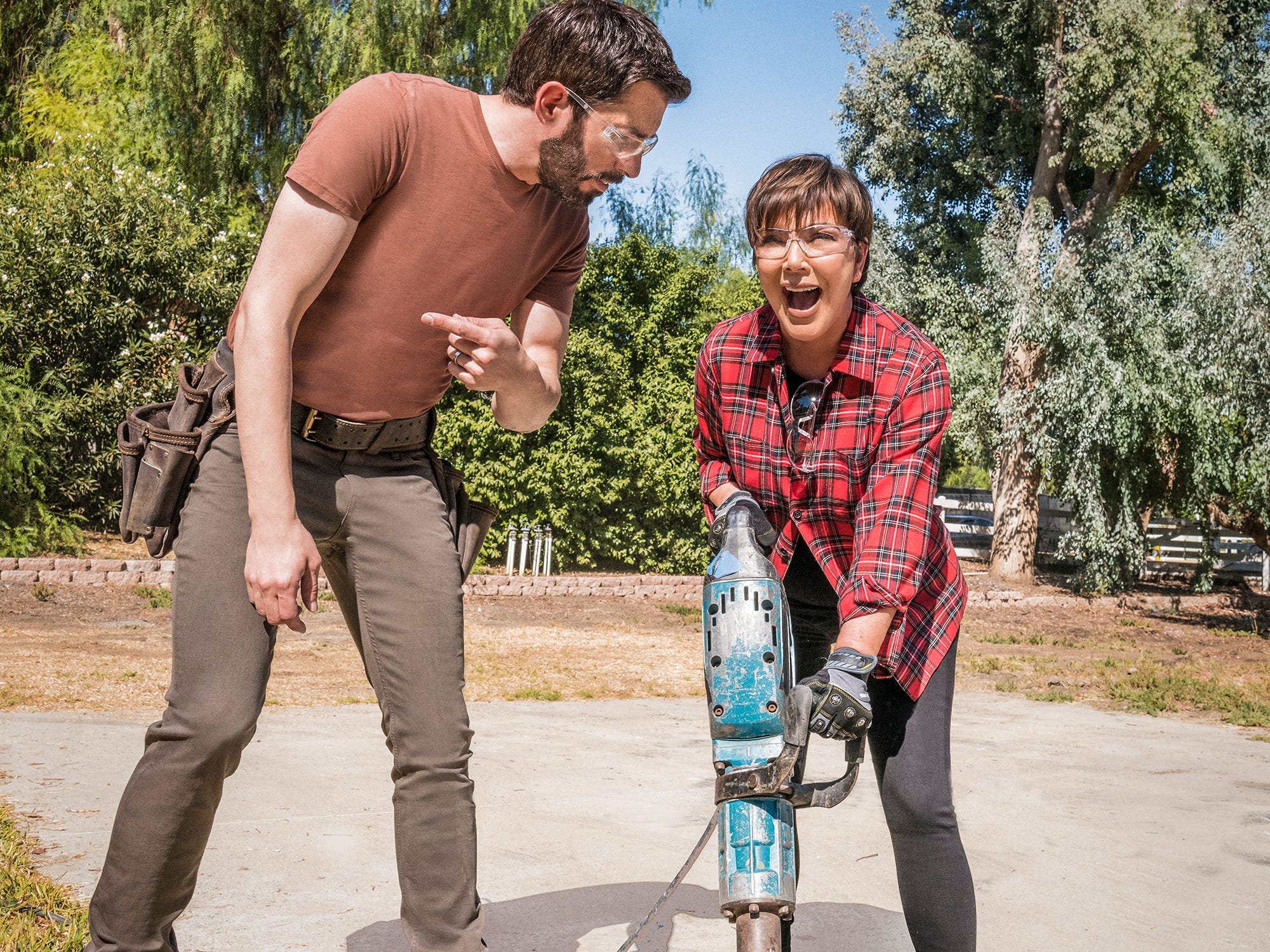 Kris Jenner uses a jackhammer while a Property Brother looks on.