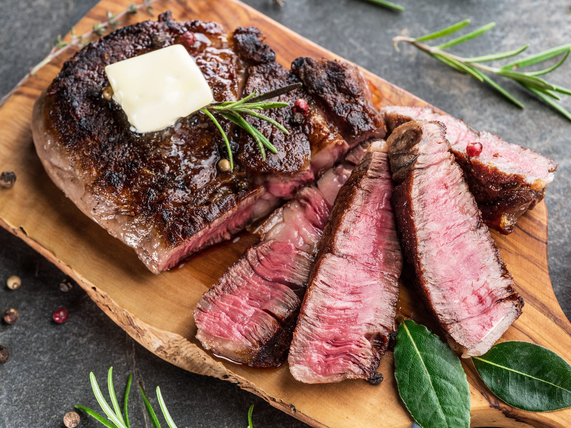 A medium-rare ribeye steak sliced on a wooden cutting board topped with a pat of butter