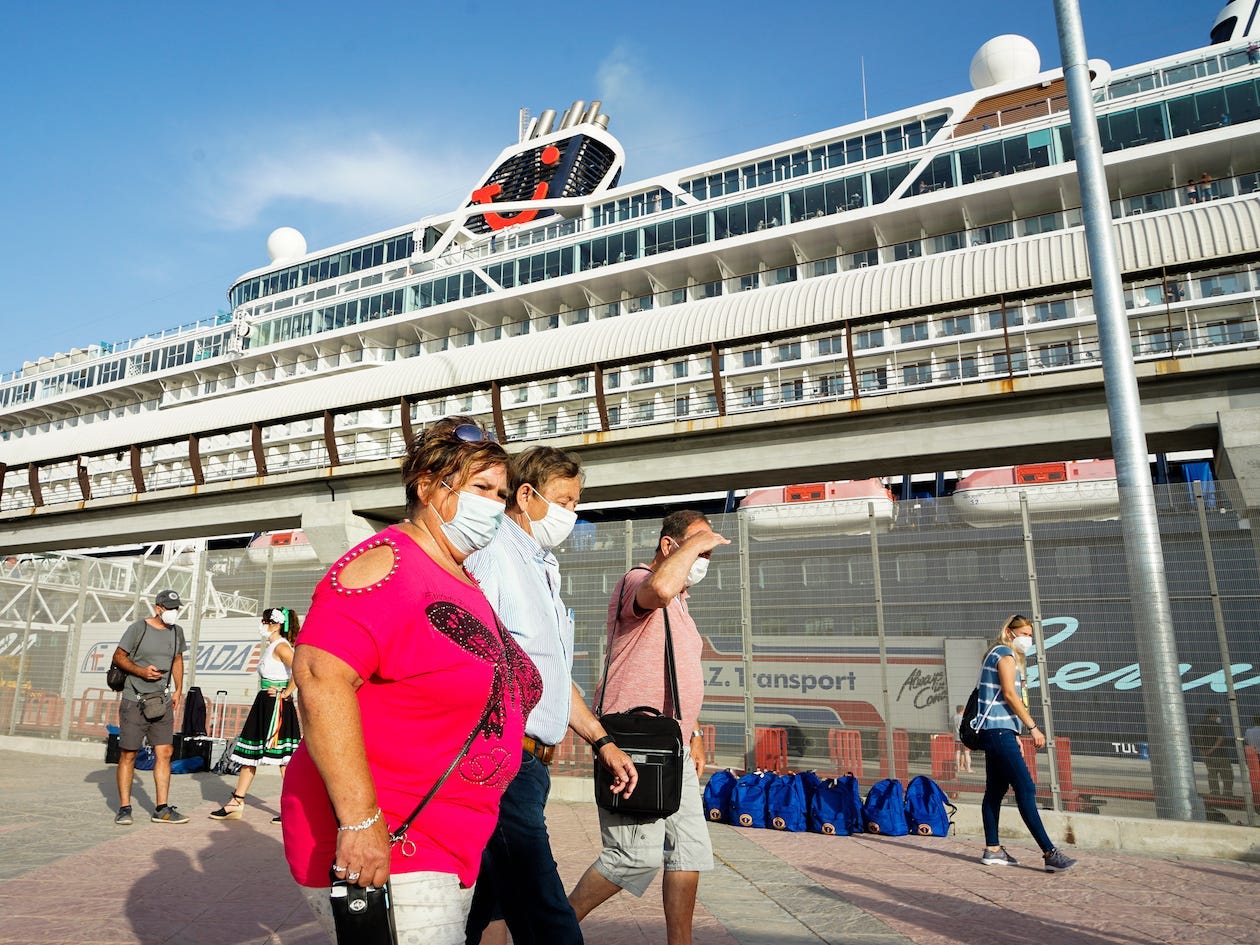 Cruise passengers walk in front of a cruise wearing masks.