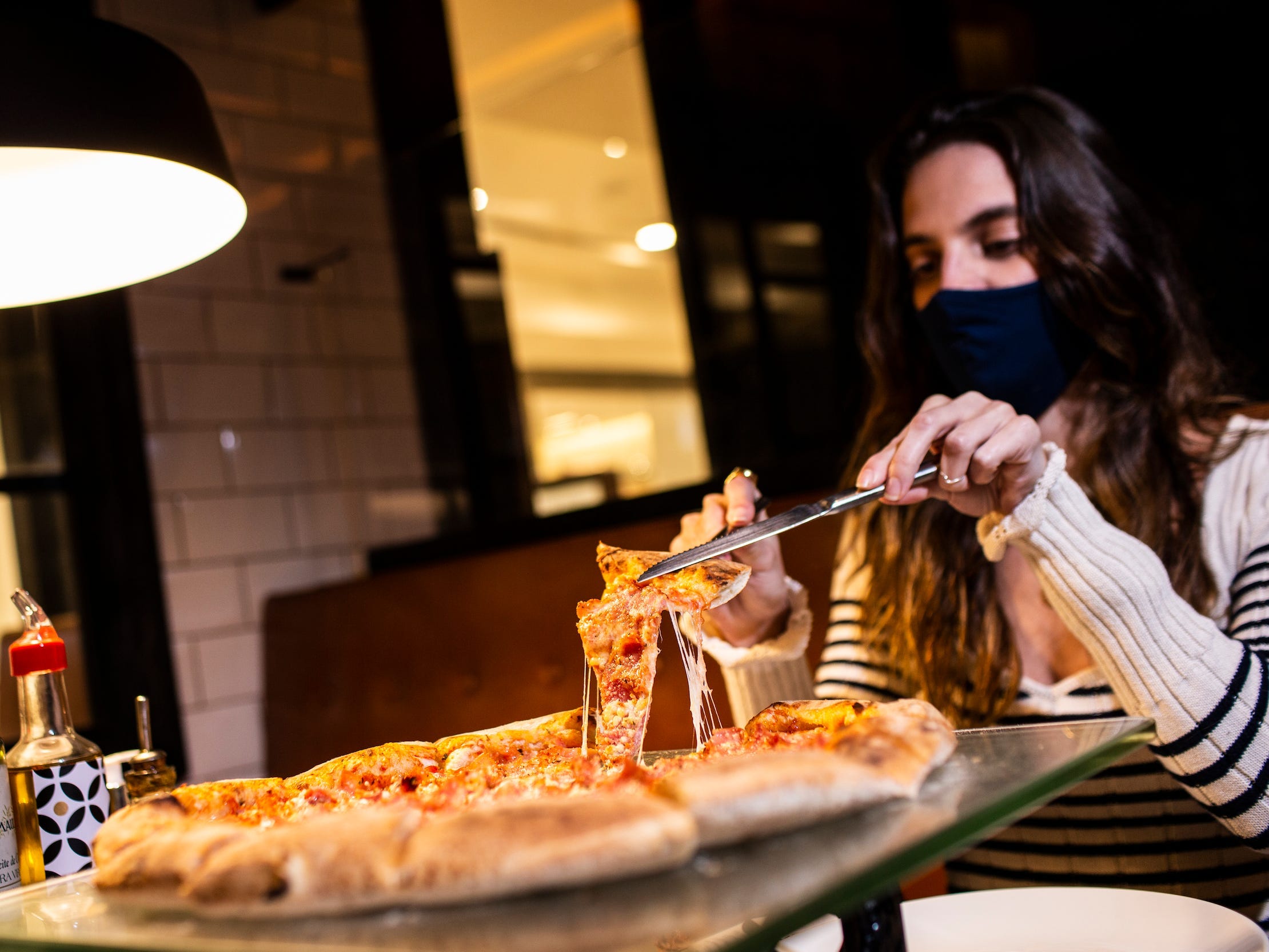 Woman in pizzeria cutting slice of pizza