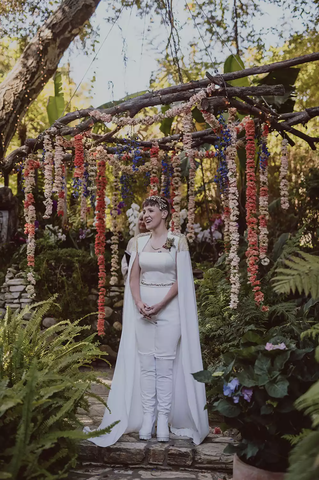 Hannah Hart wears a Pronovias pantsuit and matching cape on her wedding day.