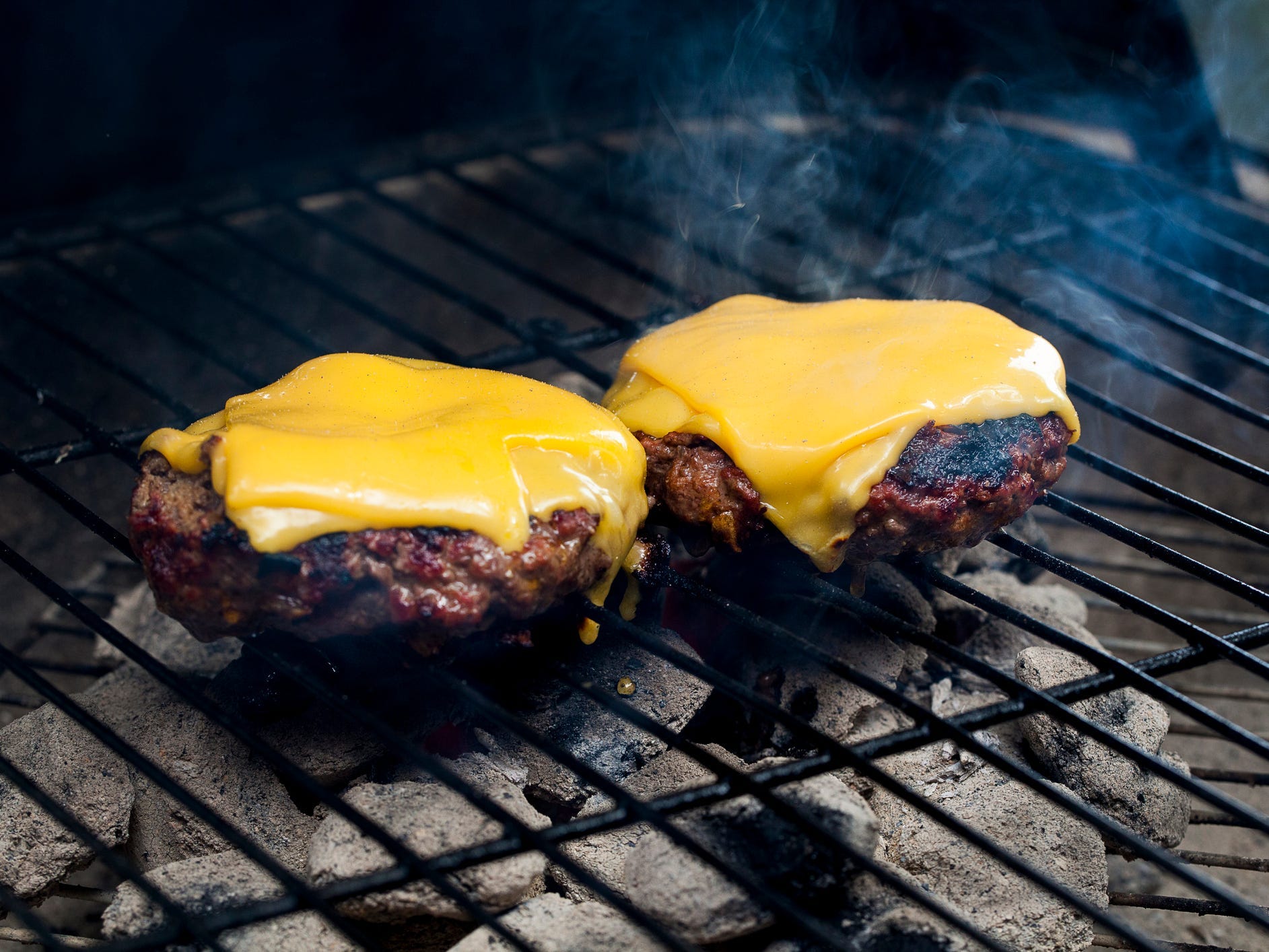 two hamburgers with melted cheese on a smoking charcoal grill