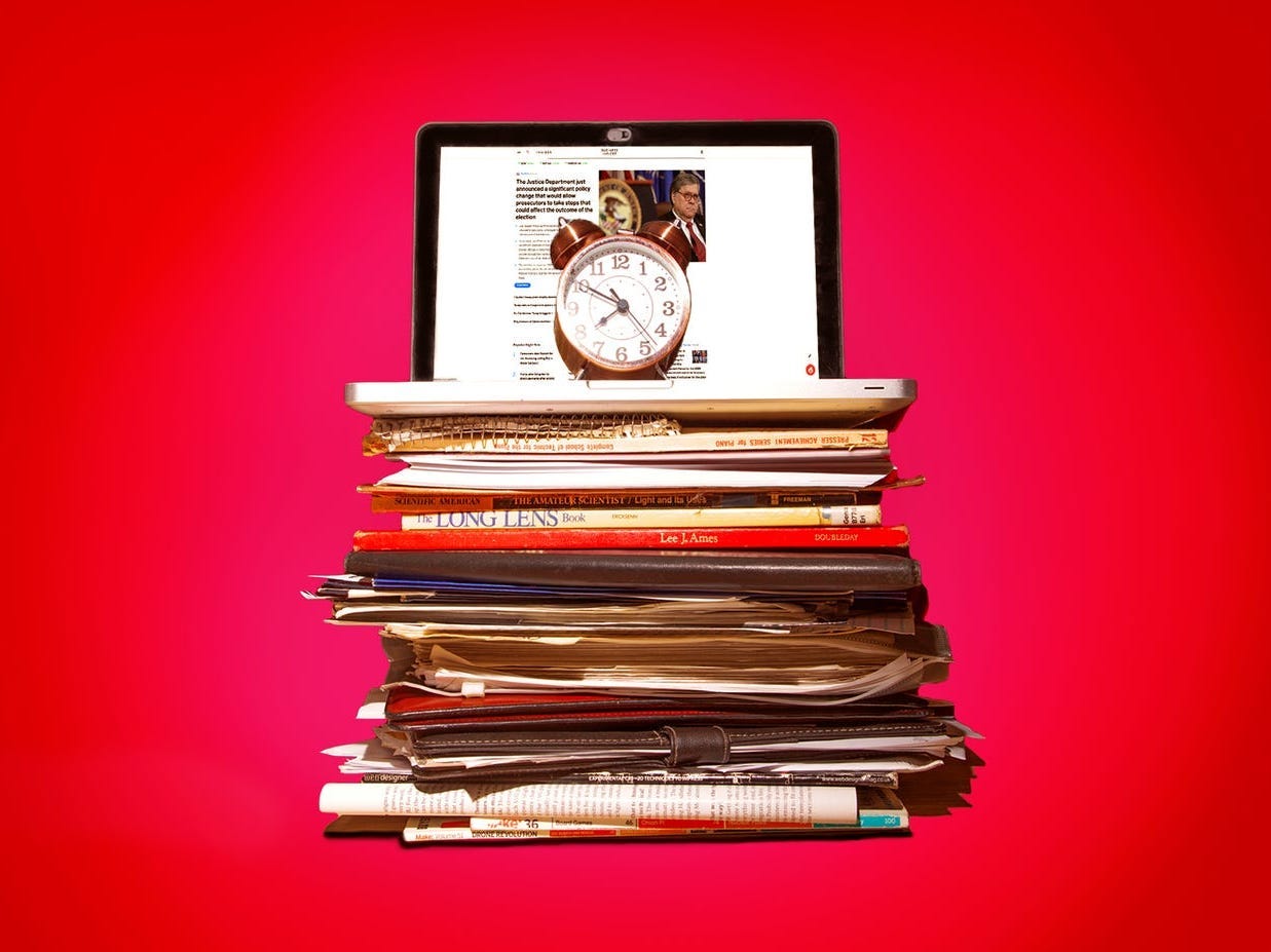 A laptop sits on top of a stack of books and papers against a red background.