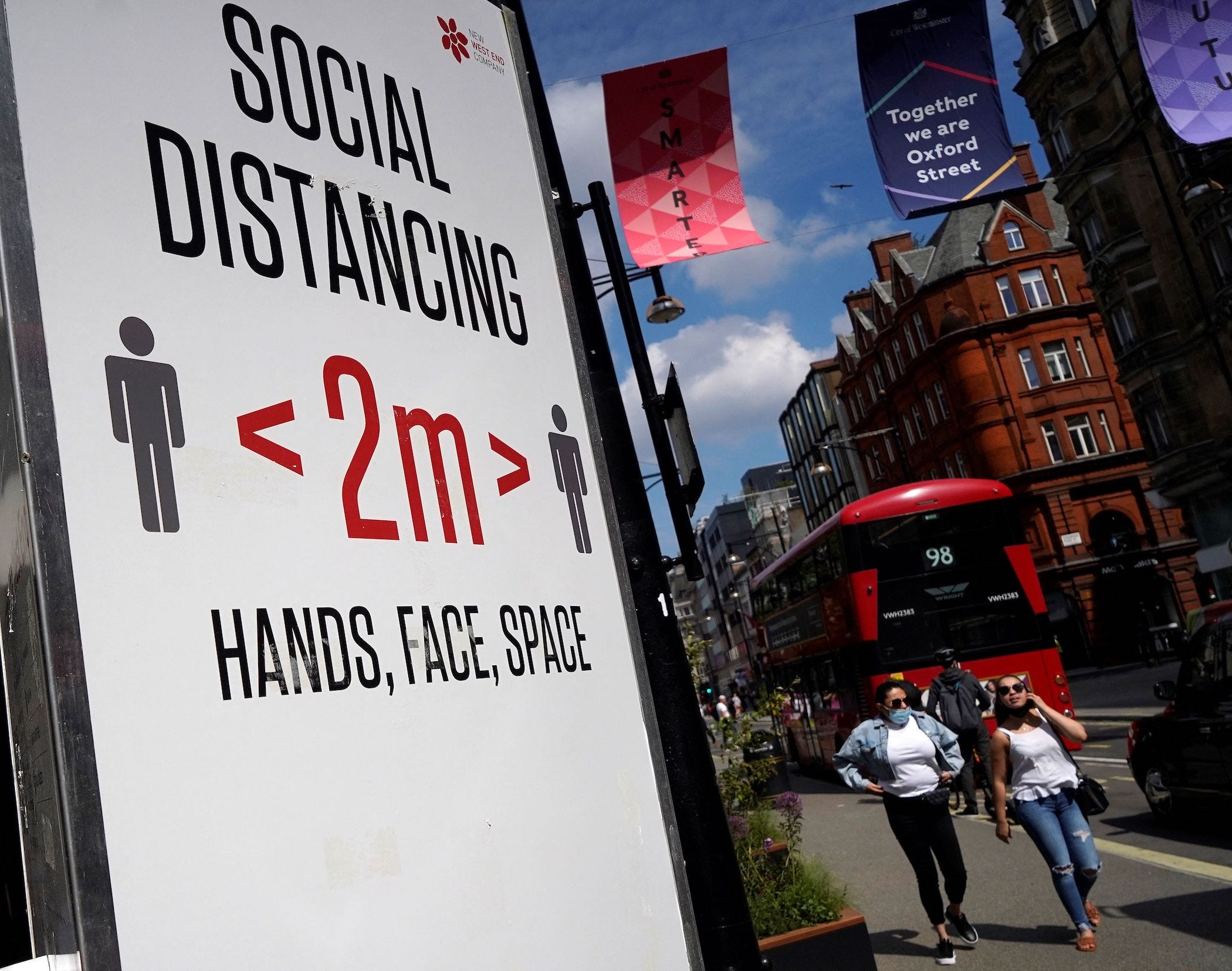 people walk past a sign on oxford street in london which encourages 2 meters of social distancing