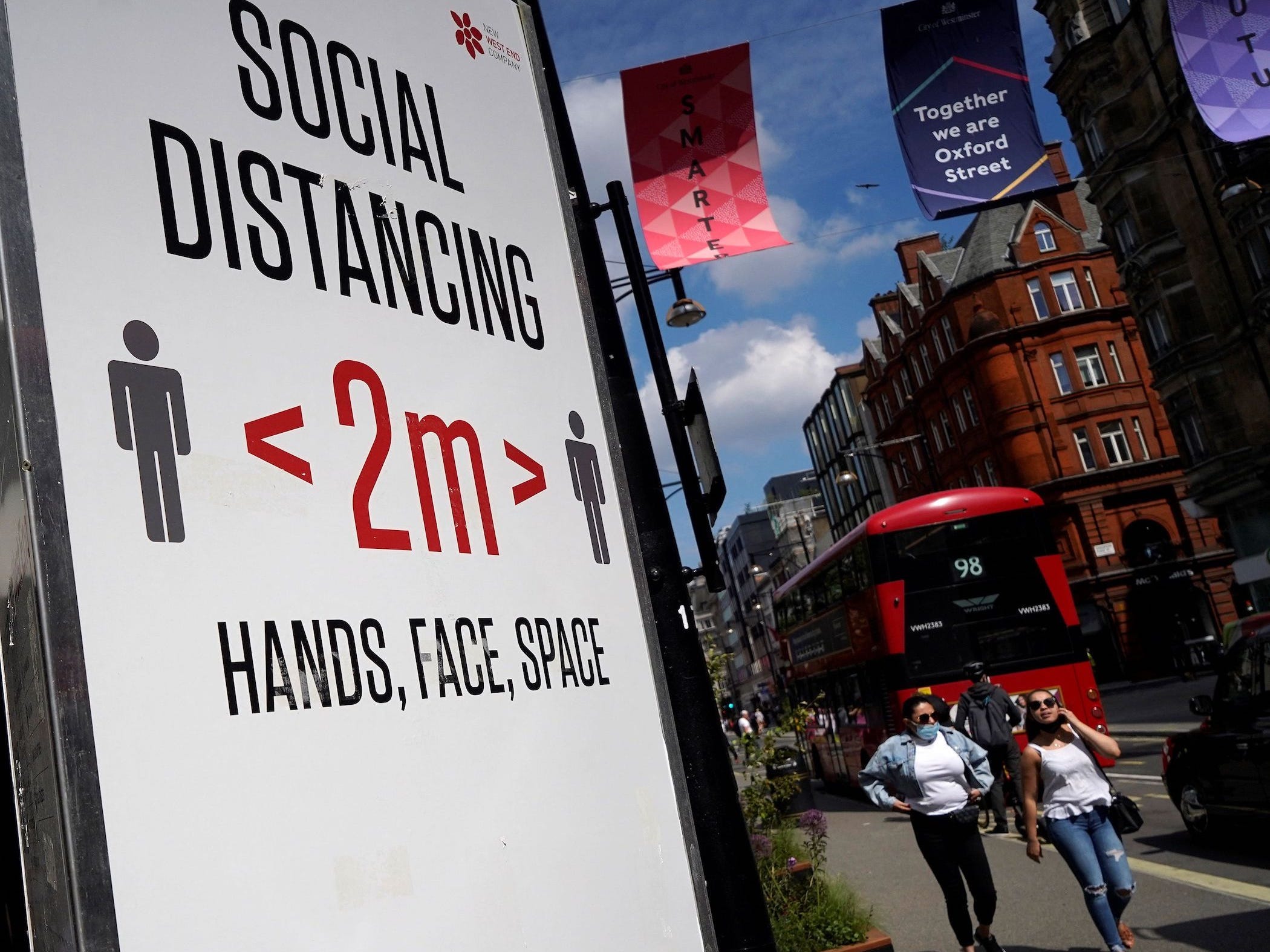 people walk past a sign on oxford street in london which encourages 2 meters of social distancing
