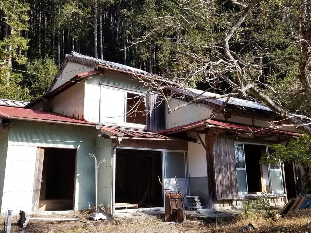 The facade of Uchiyama Seichi's countryside Akiya shows a home without window panes and surrounded by trees.