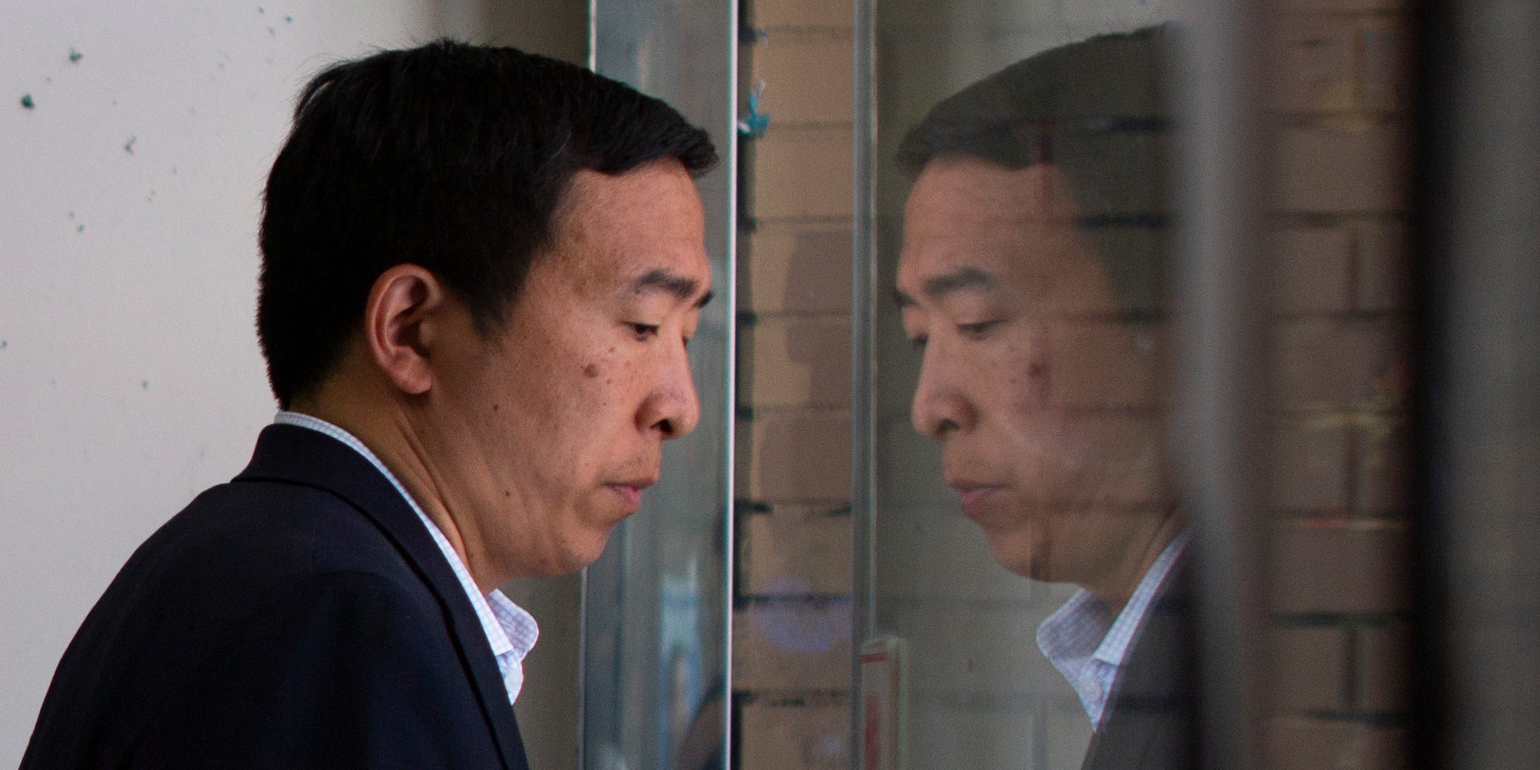 Andrew Yang walks past his reflection in a window.