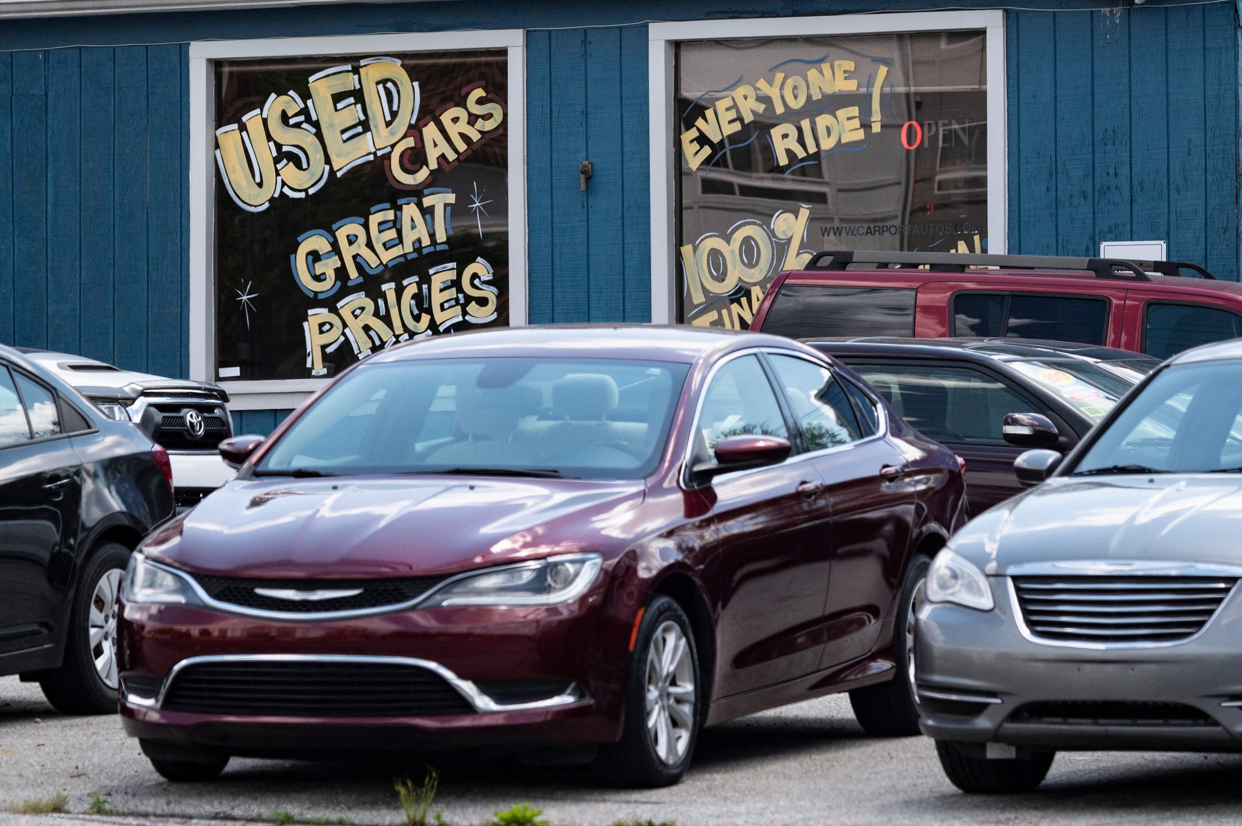 Cars sit outside a used car dealership with spray paint on the windows advertising the vehicles.