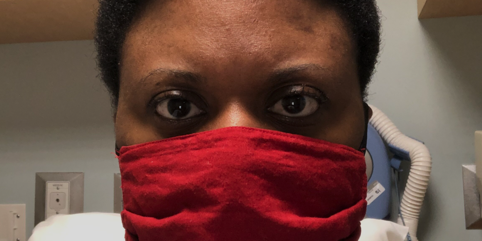 A close up picture of Chimére Smith, wearing a red mask, in the background is some medical equipment.