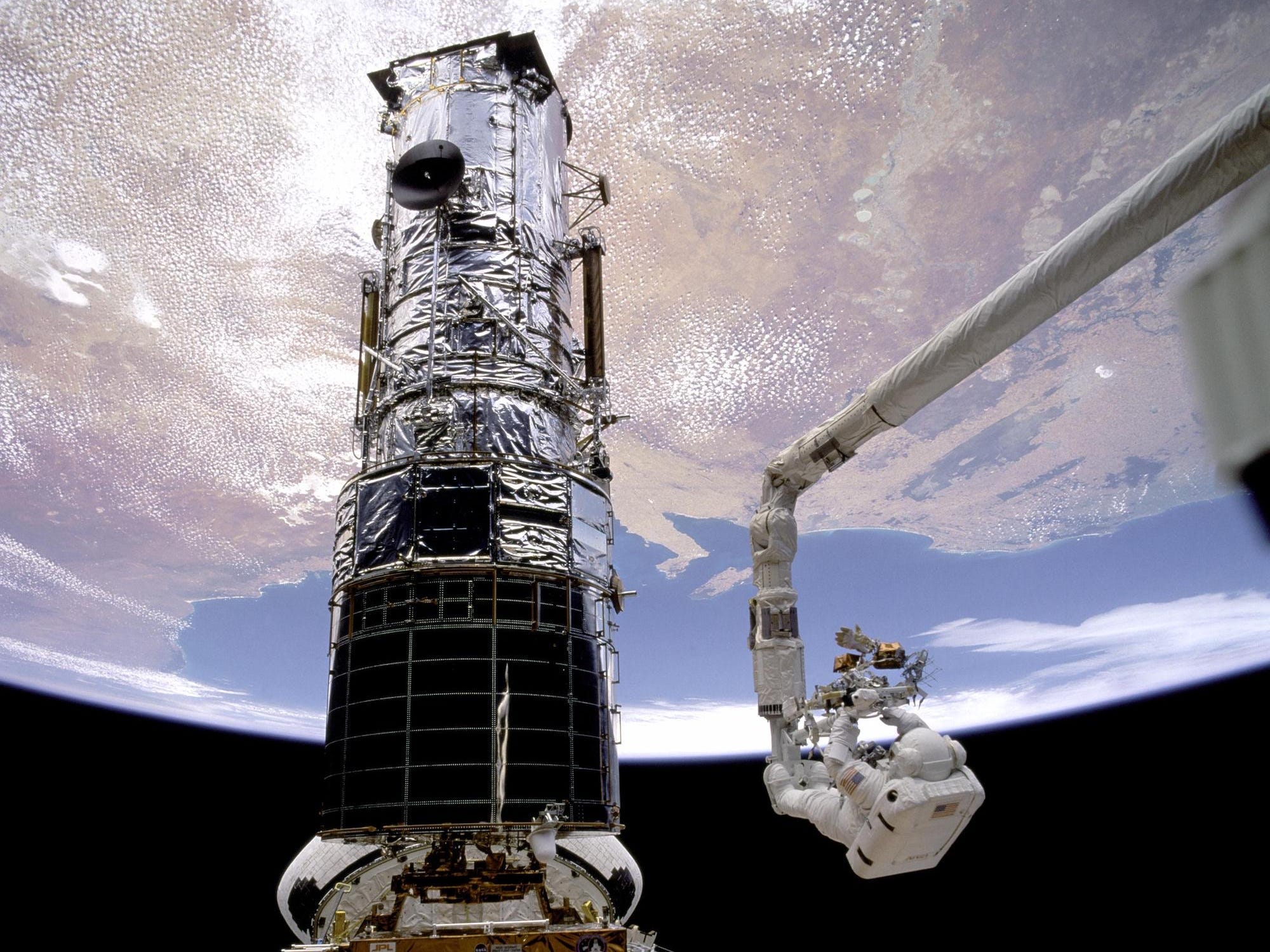 two astronauts in spacesuits work on the hubble space telescope in space above earth