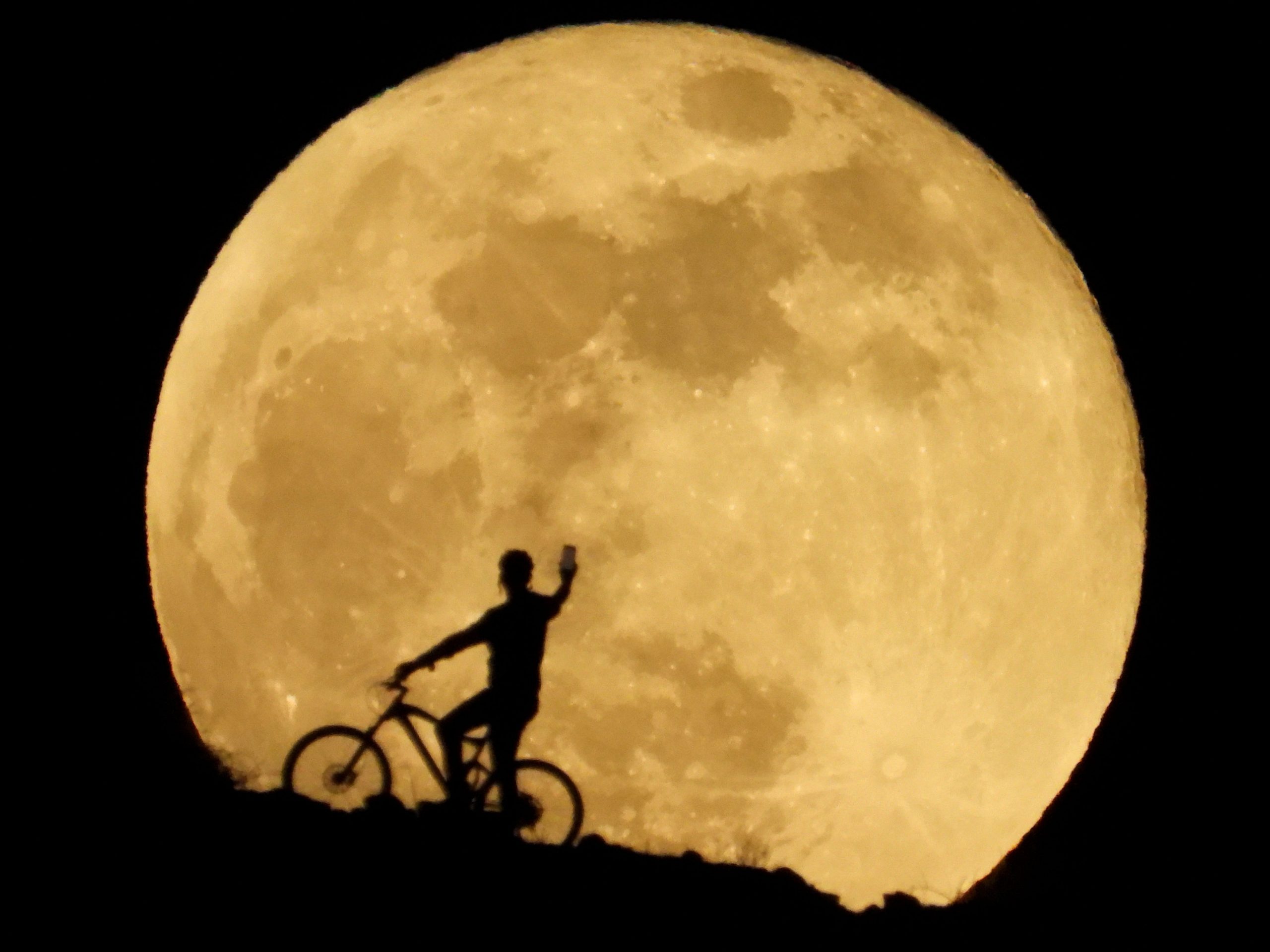supermoon rises yellow over hill where cyclist holds up cellphone