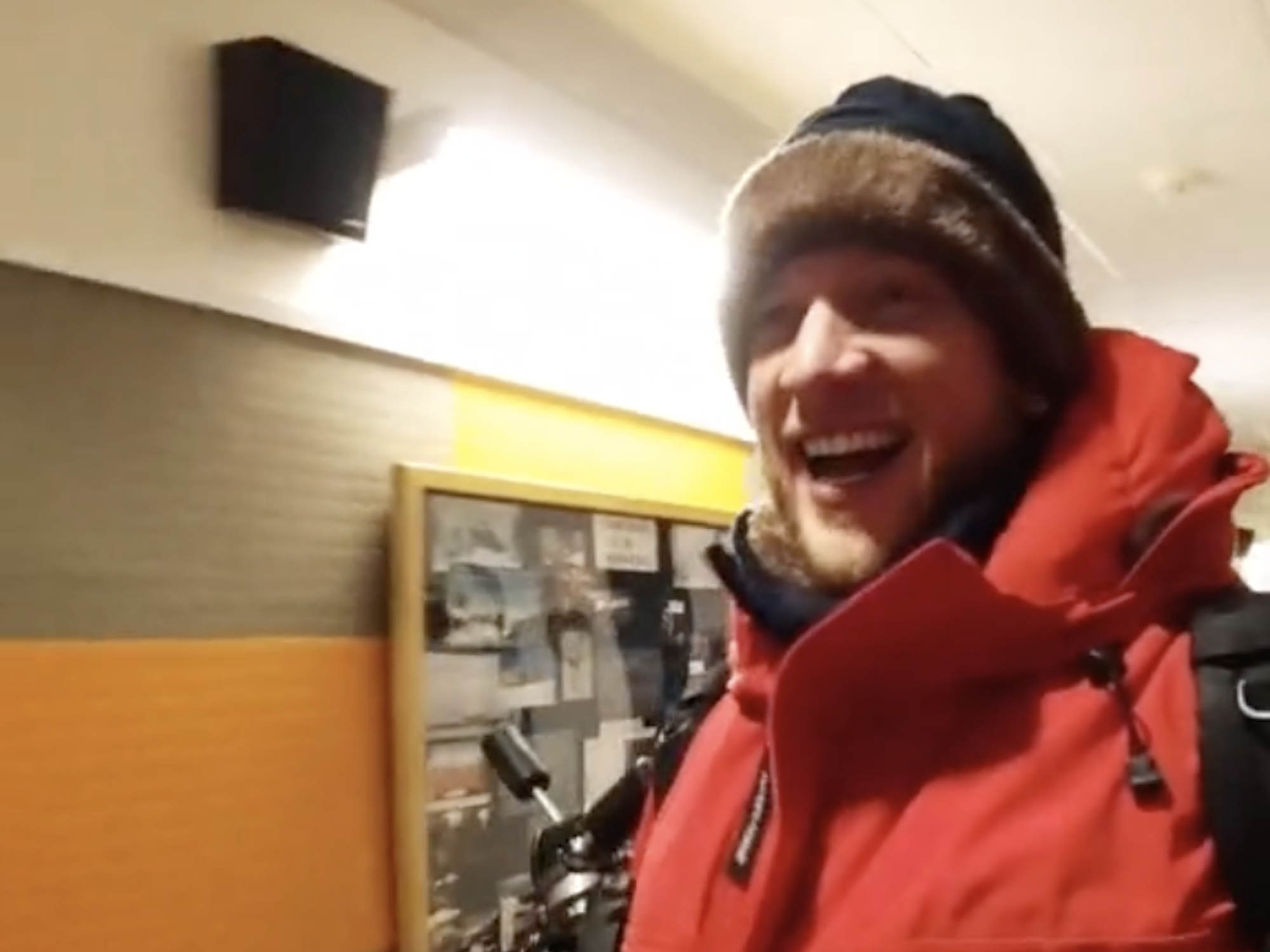 Josiah Horneman, a man, is wearing a heavy red coat whilst walking in a corridor at the Amundsen-Scott South Pole Station.